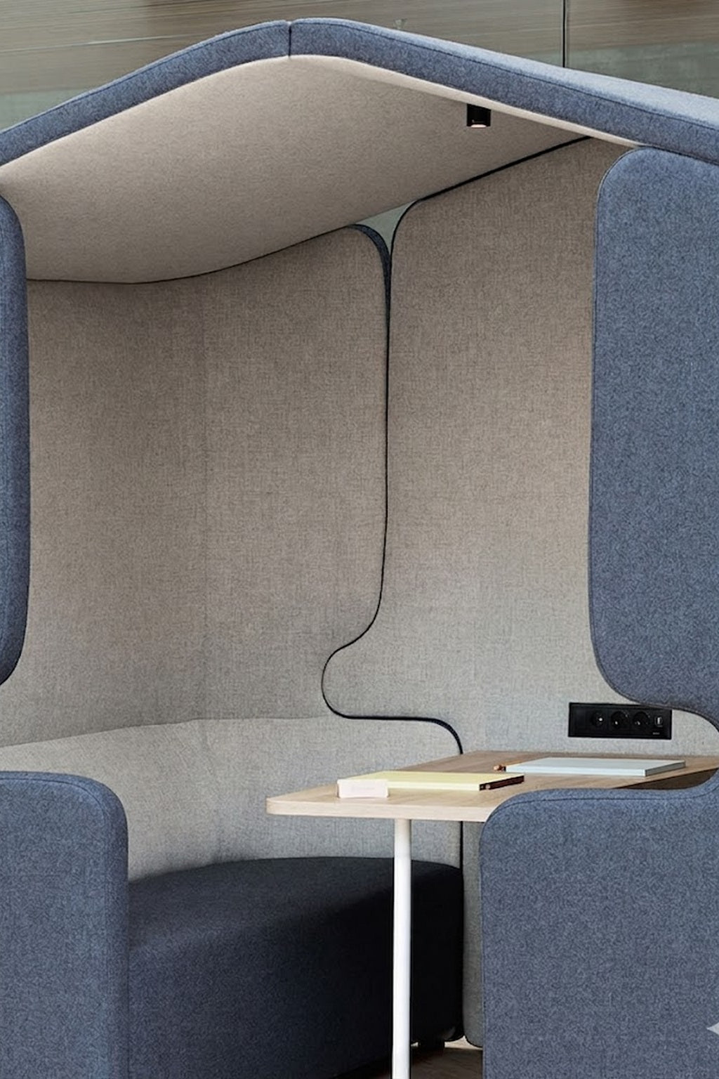 L'Alcôve acoustique Zen 4 pers bicolore + table blanche de Monsieur Bureau est un siège moderne et fermé pour quatre personnes avec un revêtement doux gris et bleu, offrant de l'intimité dans les espaces ouverts.