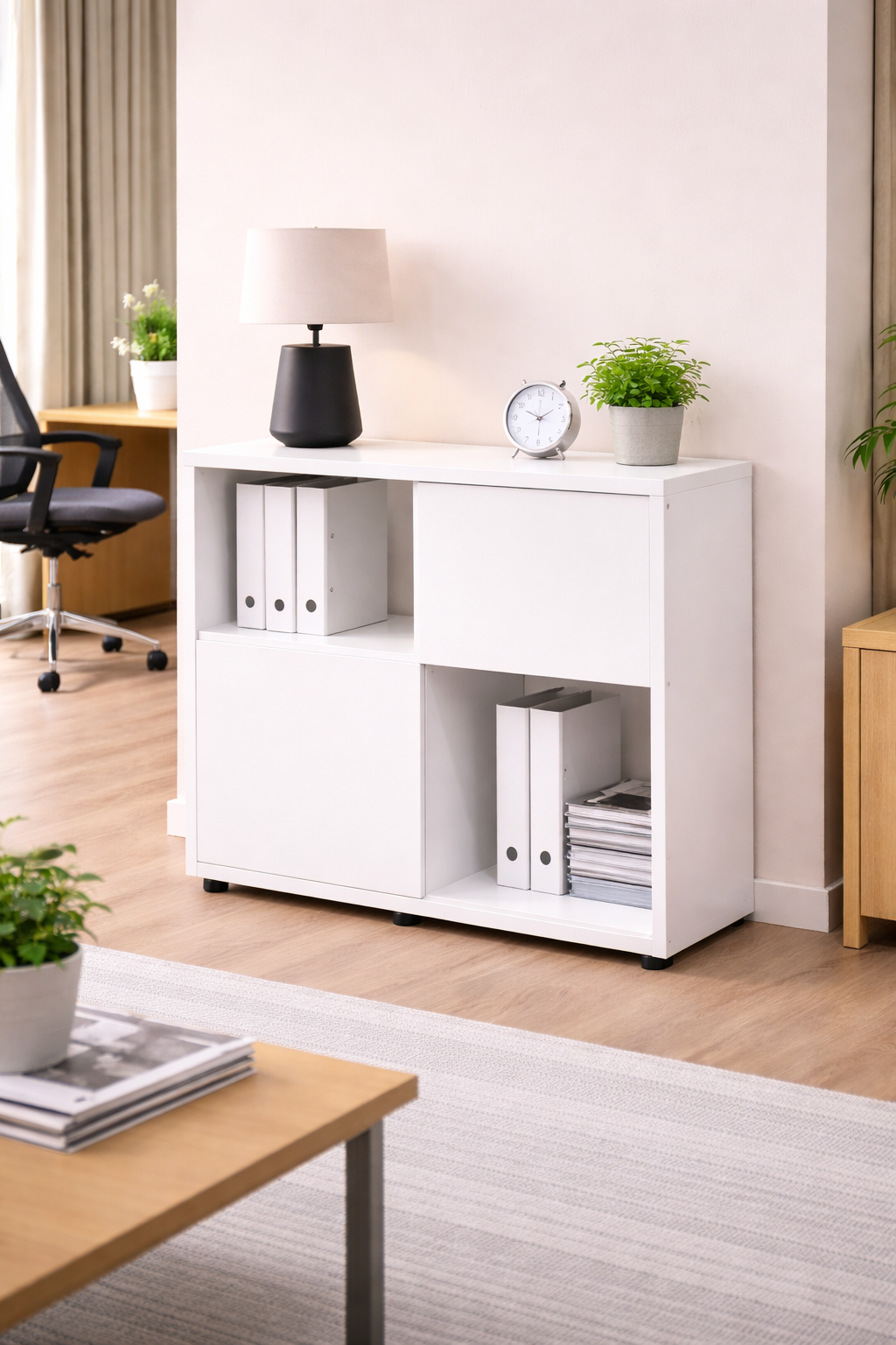 Un bureau moderne avec un Monsieur Bureau Bibliothèque Basse Curvy/Express+ 2 Portes 2 Niches blanc contient des classeurs blancs, une horloge, une lampe et deux plantes en pot. Une chaise de bureau et un bureau sont visibles à l'arrière-plan.#combo_corps_blanc_porte_blanc