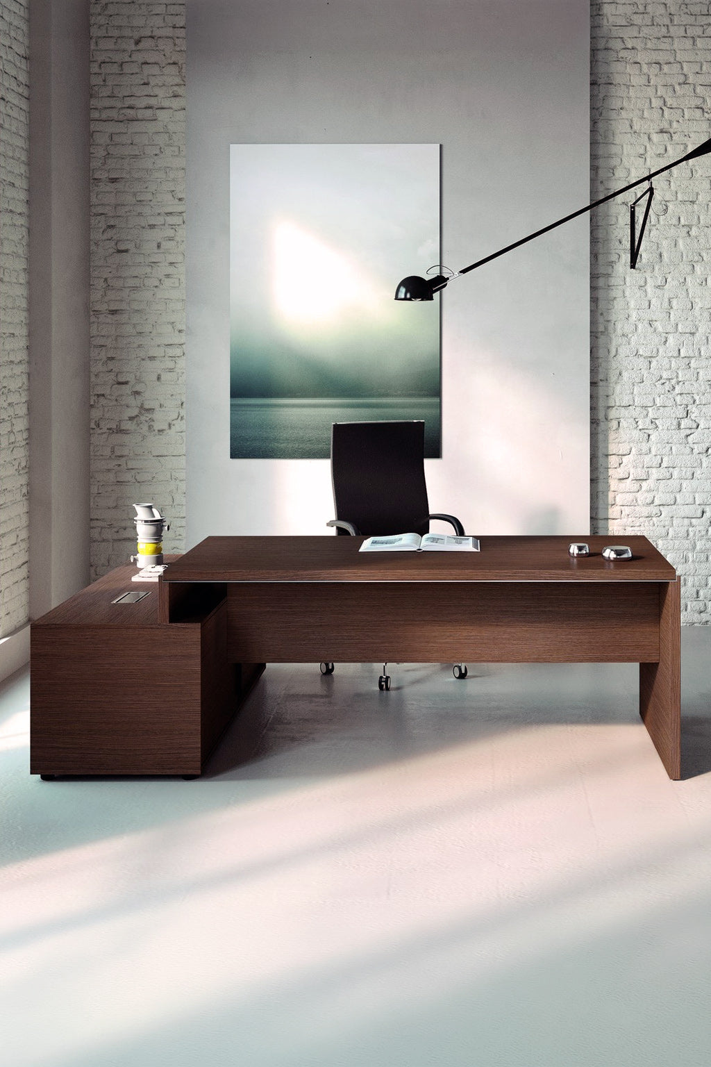 Un bureau moderne présente le bureau de direction Monsieur Bureau Asset avec retour sur crédence, une chaise pivotante noire, une lampe de bureau, des articles de bureau et une grande œuvre d'art abstraite sur un mur de briques blanches. La lumière du soleil met en valeur cet espace minimaliste d'inspiration italienne.#combo_retour_a_droite_noyer