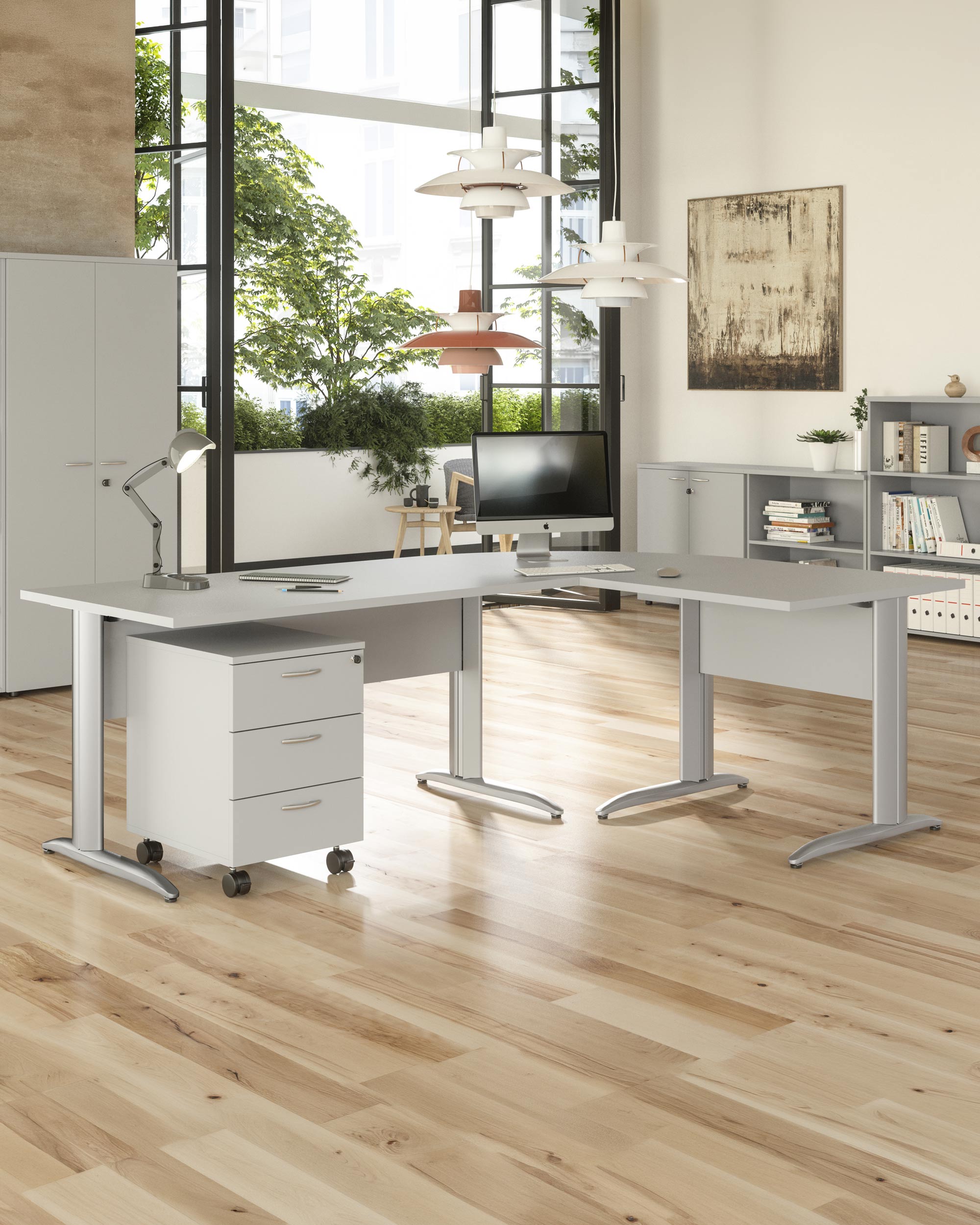 Bureau moderne doté de grandes fenêtres, d'un parquet en bois clair et d'un Bureau Pro Effect Droit ou Angle Modulable de Monsieur Bureau. Des bureaux blancs, un tiroir de rangement roulant, une lampe de bureau et des étagères avec des livres complètent le design d'inspiration italienne.