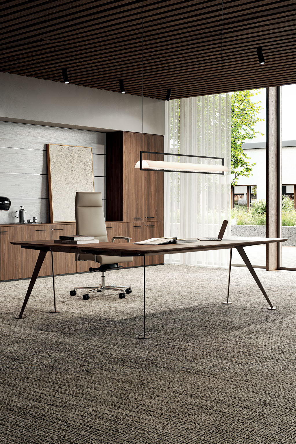 Le Bureau de direction Spike placage bois avec retour de Monsieur Bureau est composé d'un bureau élégant, d'une chaise de direction, d'un ordinateur portable fermé, de papiers éparpillés, d'une finition en bois de première qualité, de grandes fenêtres avec des rideaux diaphanes et d'une lumière naturelle abondante.