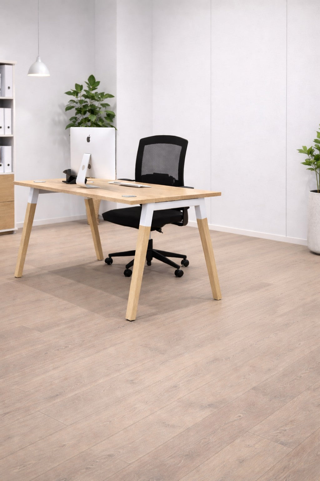 Le Bureau professionnel individuel Oslo P70 P80 cm de Monsieur Bureau est composé d'un bureau en bois, d'une chaise en maille noire, d'un écran d'ordinateur, de plantes vertes en pot et d'étagères avec des classeurs blancs dans un design scandinave sur un mur clair.