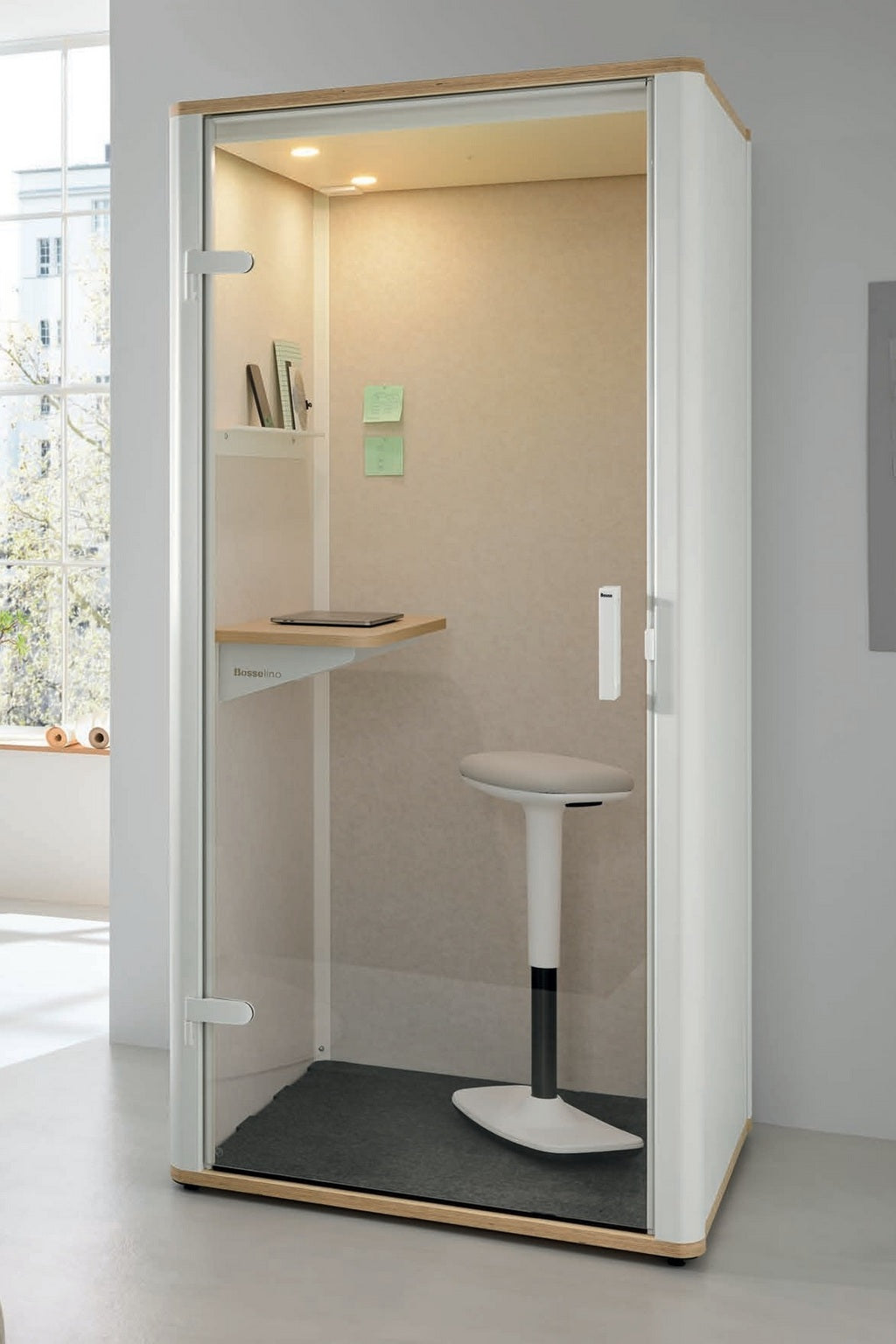 La Cabine acoustique Silen - Phone booth 1 personne de Monsieur Bureau est composée de parois en verre, d'un petit bureau, d'un tabouret blanc haut, d'étagères et de notes adhésives dans une pièce lumineuse, idéale pour votre espace de concentration.