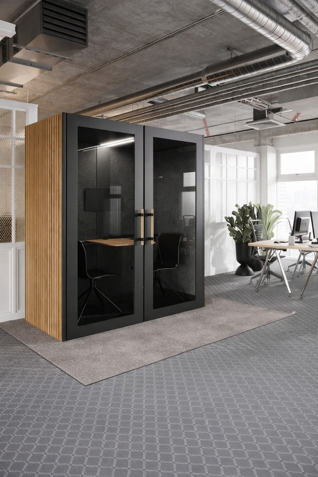 Un bureau ouvert moderne présente le Monsieur Bureau Cabine Acoustique Double No Sound Executive 2 pers - avec bureau et chaise sur moquette - ainsi que des plafonds apparents, de grandes fenêtres, des bureaux et une plante en arrière-plan.
