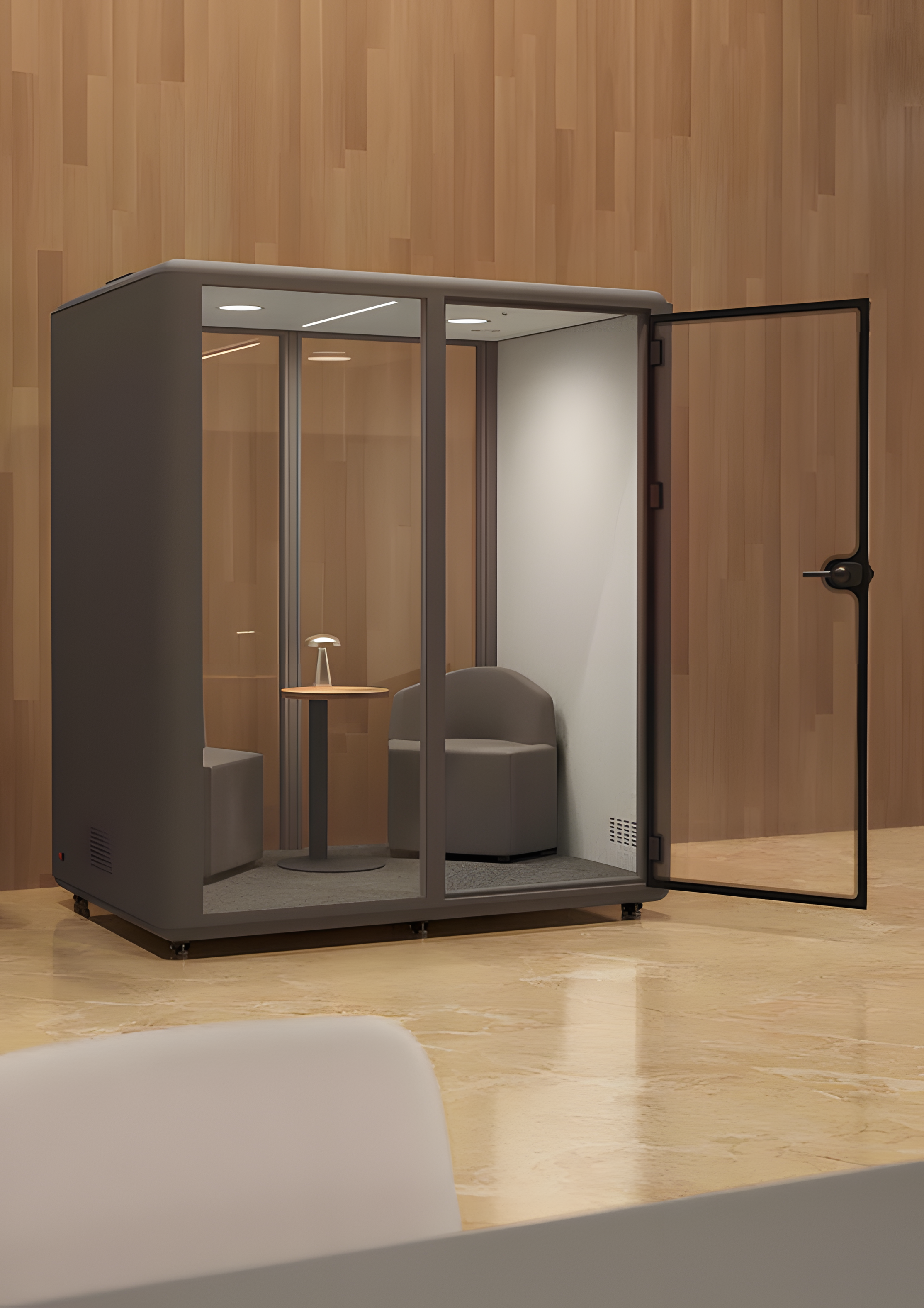 La Cabine acoustique Aura M Meet 2 personnes de Monsieur Bureau se compose de parois en verre, d'une porte ouverte, de deux chaises grises et d'une petite table ronde avec une lampe, le tout contre un mur lambrissé et un sol clair.