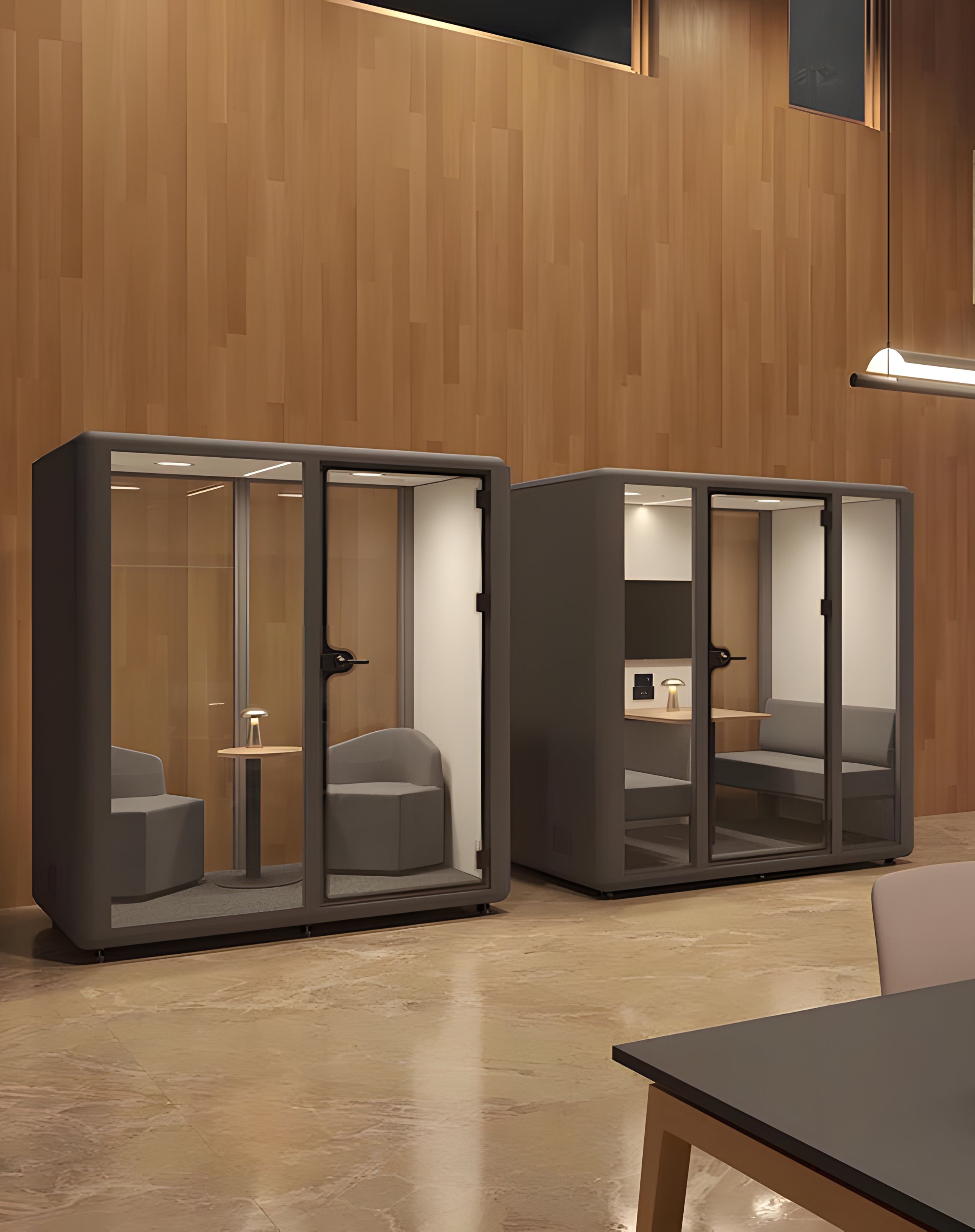 Deux Cabines acoustiques Aura M Meet 2 personnes de Monsieur Bureau, chacune équipée de chaises et d'un bureau, sont adossées à un mur en bois dans une pièce lumineuse au sol en marbre, offrant une isolation acoustique optimale.