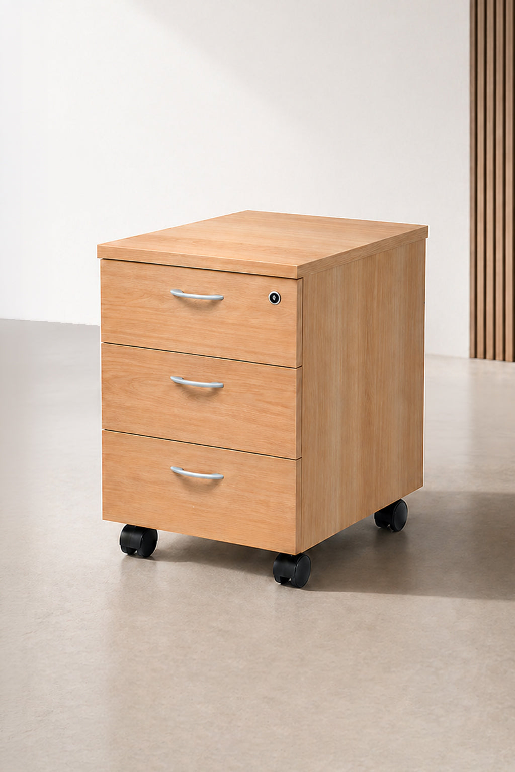 Le Caisson mobile Budget / Effect 2 ou 3 tiroirs de Monsieur Bureau, en bois clair avec poignées argentées et roulettes noires, offre un rangement intelligent sur un sol beige sur fond neutre.#combo_chene_3_tiroirs