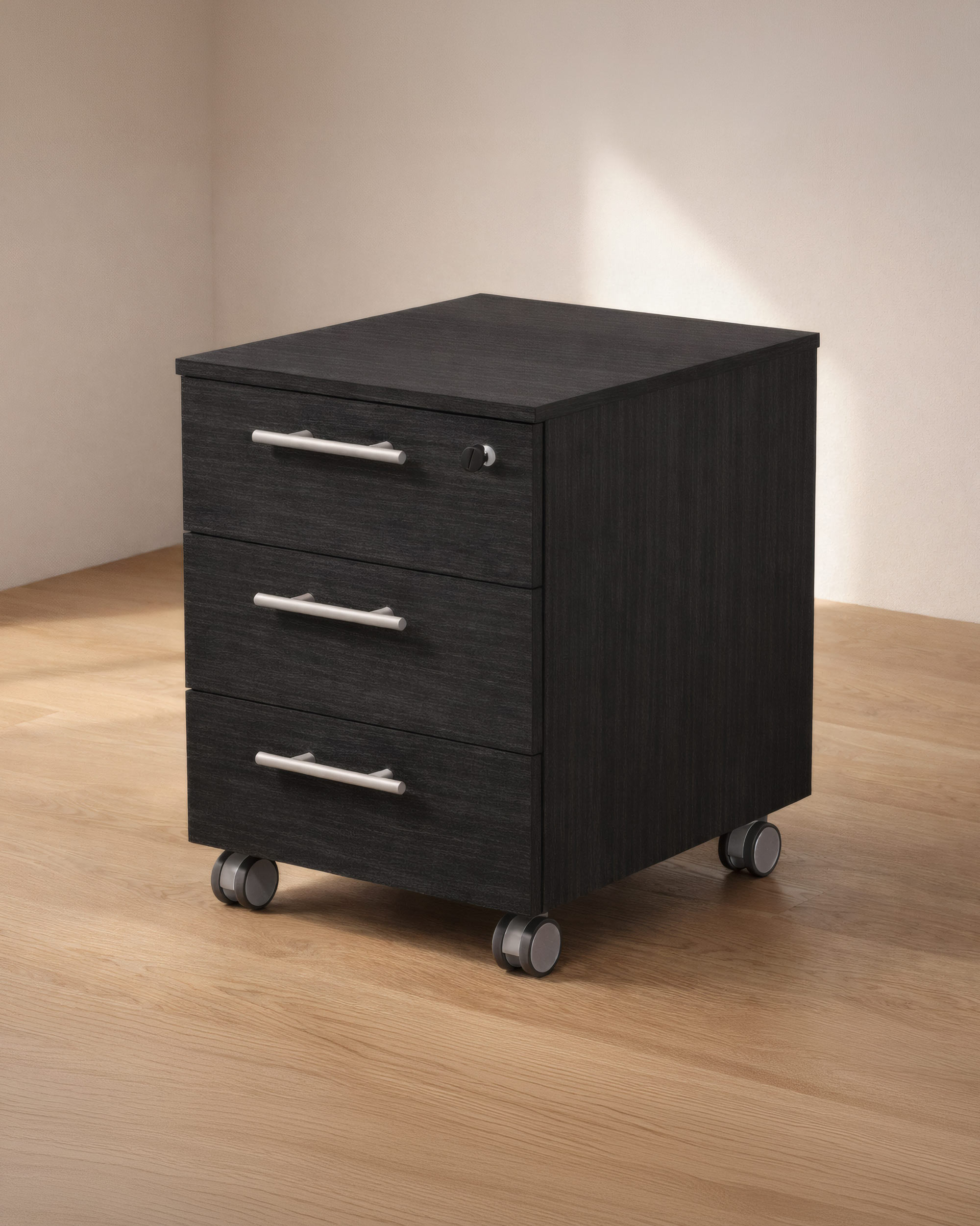 Le Caisson mobile professionnel Flora 3 tiroirs de Monsieur Bureau, fabriqué en matériaux recyclés noirs avec des poignées argentées et quatre roues, offre un rangement bureau pratique dans un coin sur un sol en bois clair.#finitions_frene_noir