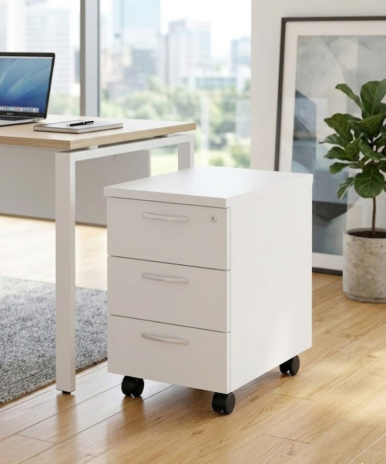 Un classeur Monsieur Bureau Caisson Mobile Curvy / Express+ à trois tiroirs sur roulettes se trouve à côté d'un bureau moderne avec des planchers en bois, une grande fenêtre, une plante en pot et des œuvres d'art encadrées en arrière-plan.#combo_3_tiroirs_blanc