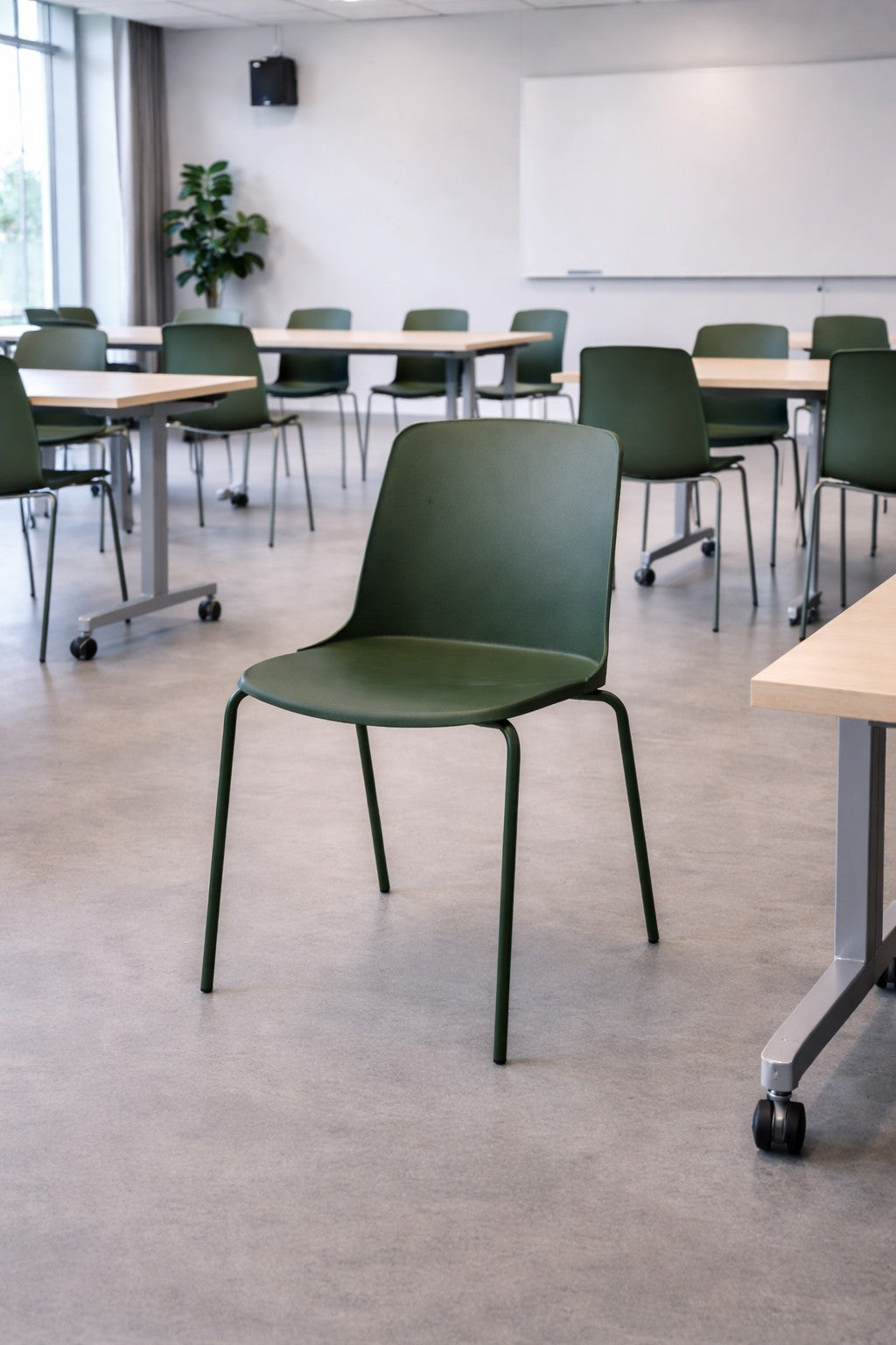 Une chaise empilable ALIX de Monsieur Bureau trône au centre d'une salle de classe moderne et lumineuse, entourée de chaises et de tables assorties. Un tableau blanc, une plante et de grandes fenêtres complètent cet élégant mobilier professionnel.