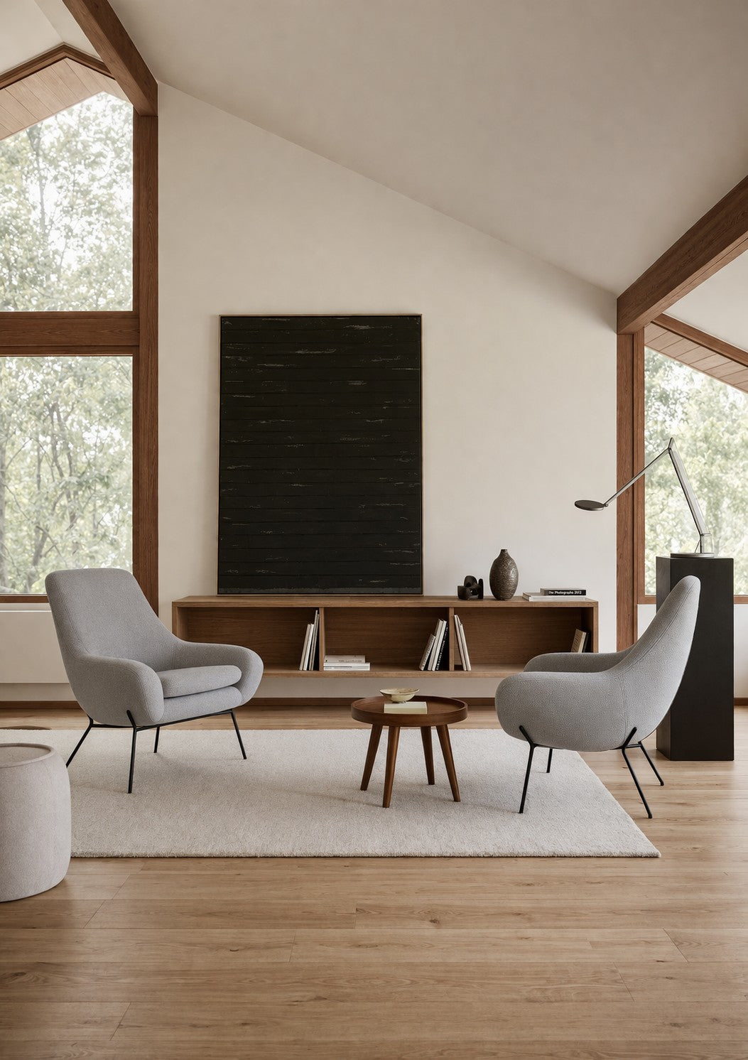 Un salon moderne avec deux chaises Fauteuil Lounge Nomi de Susanne GRØNLUND pour Monsieur Bureau, une table basse ronde en bois, un tapis beige et une console. De grandes fenêtres inondent l'espace minimaliste de lumière et de vues sur les arbres pour une atmosphère calme.