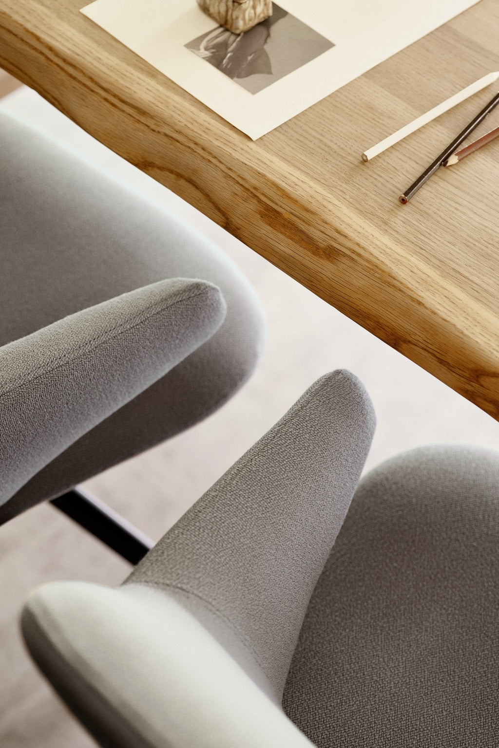 Deux chaises modernes gris clair Fauteuil pivotant design KAPP - Tissu Vision Gris de Monsieur Bureau sont assises à côté d'une table en bois. Sur la table se trouvent des crayons et une petite gravure d'art avec une sculpture en pierre pour un look minimal et confortable.