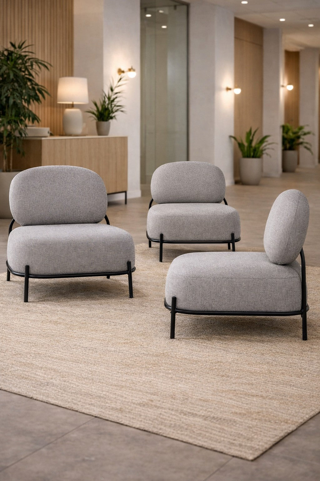 Trois chaises modernes grises Fauteuil d'accueil Brooklin - Pieds métal de Monsieur Bureau sont posées sur un tapis beige dans une pièce spacieuse et contemporaine agrémentée de plantes en pot, d'un buffet et d'un éclairage doux pour un design minimaliste.