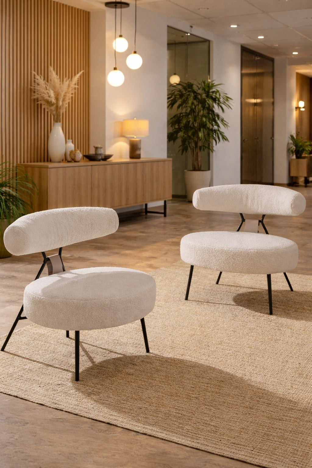 Deux chaises Monsieur Bureau Fauteuil d'accueil professionnel TED en blanc avec des pieds en métal noir sont posées sur un tapis beige dans une pièce élégante et minimaliste avec des accents en bois, des plantes et une lumière chaude provenant de lampes globe suspendues.