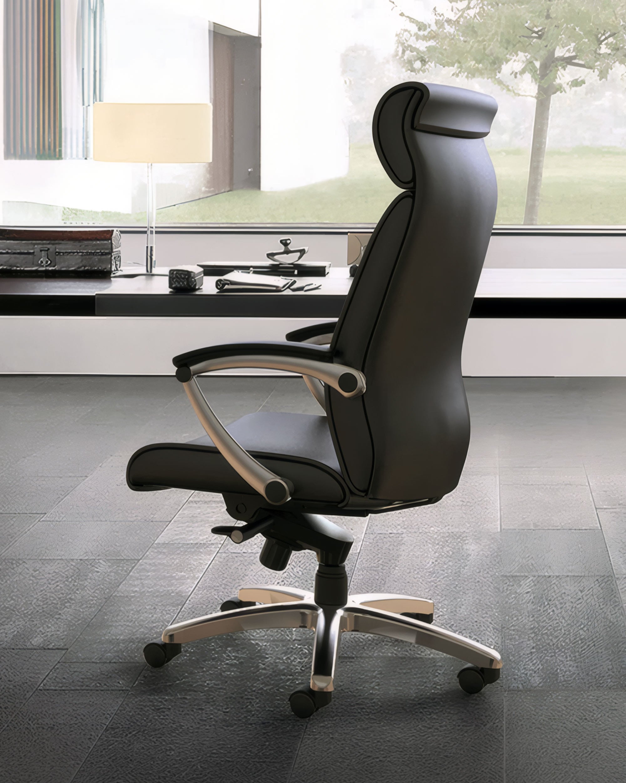 Le fauteuil de direction cuir Hydri à mécanisme synchrone de Monsieur Bureau, noir avec accoudoirs et roulettes, est positionné latéralement devant un élégant bureau, face à une grande fenêtre offrant une vue extérieure.#finitions_noir