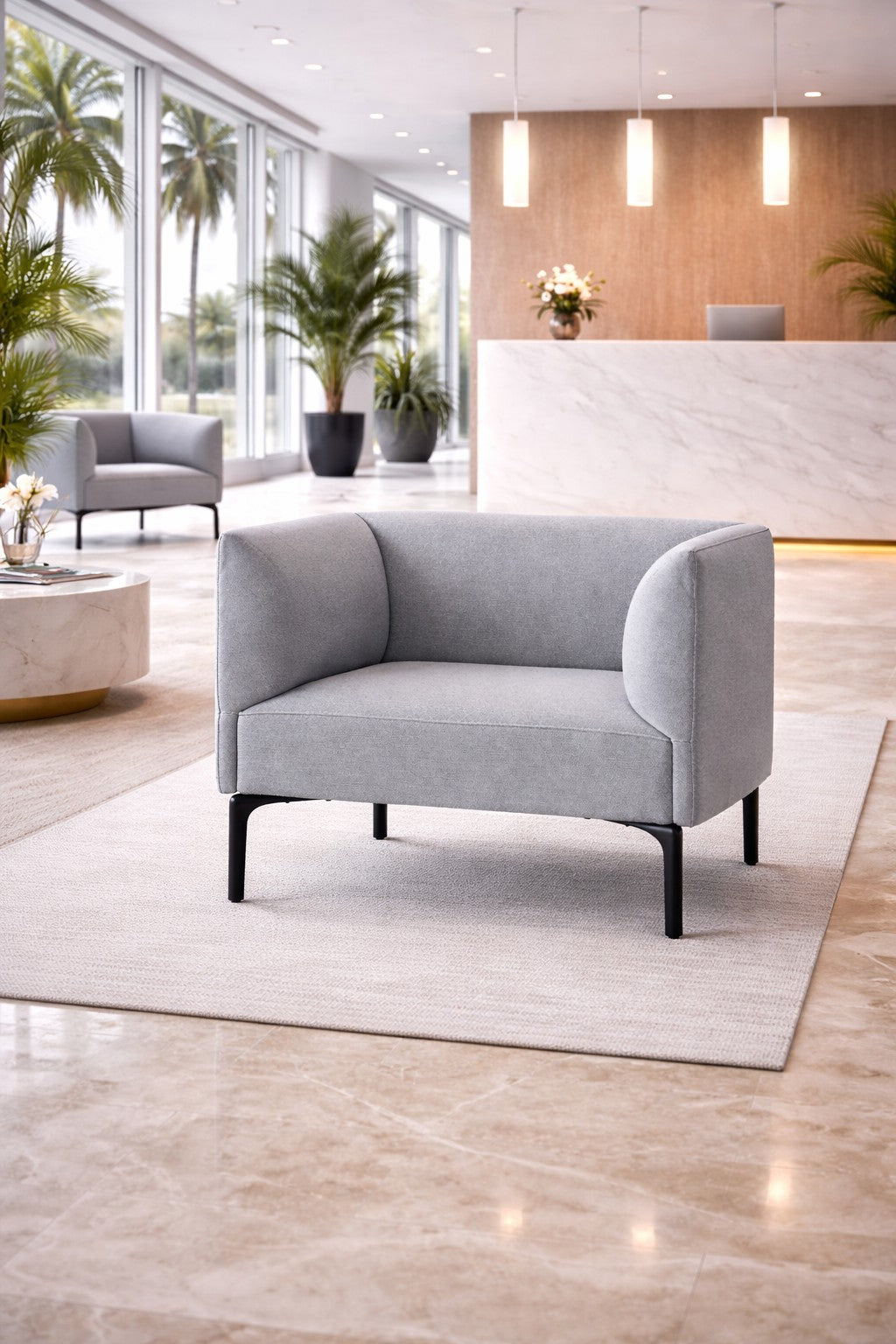 Un hall moderne avec le Fauteuil d'accueil Kay de Monsieur Bureau en gris clair sur un tapis beige, un sol en marbre, des plantes en pot, de grandes fenêtres avec vue sur les palmiers, et un bureau de réception en marbre avec des lampes suspendues et des fleurs.