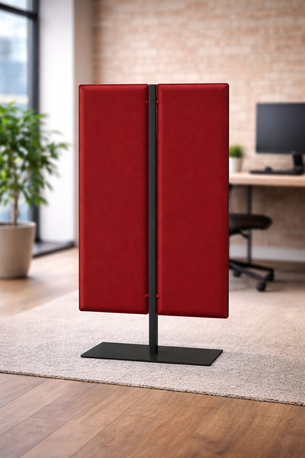 Une Cloison acoustique Aria H140/H160/H180 de Monsieur Bureau, un panneau acoustique rouge autoportant avec une base en métal noir, est placée dans un bureau moderne avec des planchers en bois, un bureau, une chaise, un ordinateur et une plante en pot pour améliorer l'isolation acoustique.#finitions_rouge