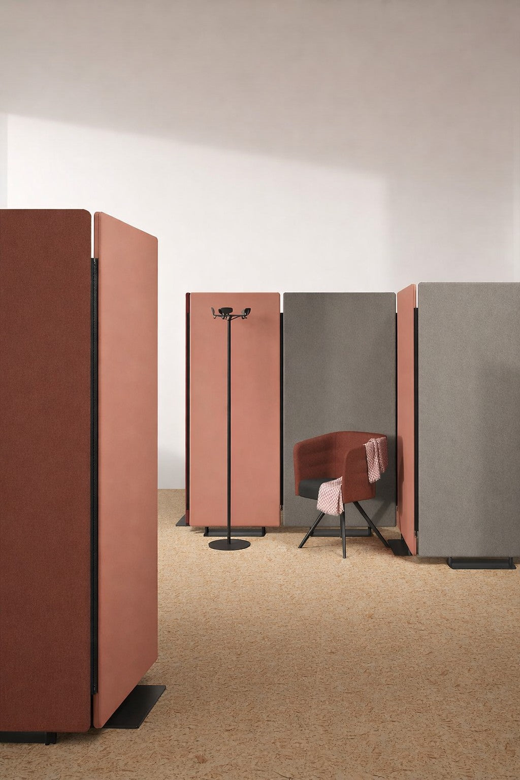 Un espace ouvert moderne présente un grand Cloison Acoustique Silenza H160 rouge et gris avec Zip de Monsieur Bureau pour le confort acoustique, une chaise de bureau rouge assortie avec une écharpe, et un porte-manteau noir sur un sol en liège clair baigné de lumière naturelle.