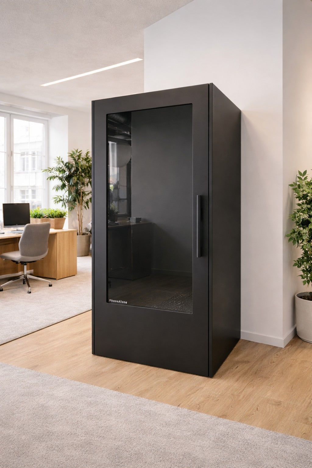 Un bureau ouvert moderne avec la cabine téléphonique acoustique NO SOUND Standard 1 personne de Monsieur Bureau, en noir avec une porte en verre pour l'isolement phonique supérieur, placée près de bureaux, de chaises, de grandes fenêtres et de plantes vertes en pot.#finitions_noir