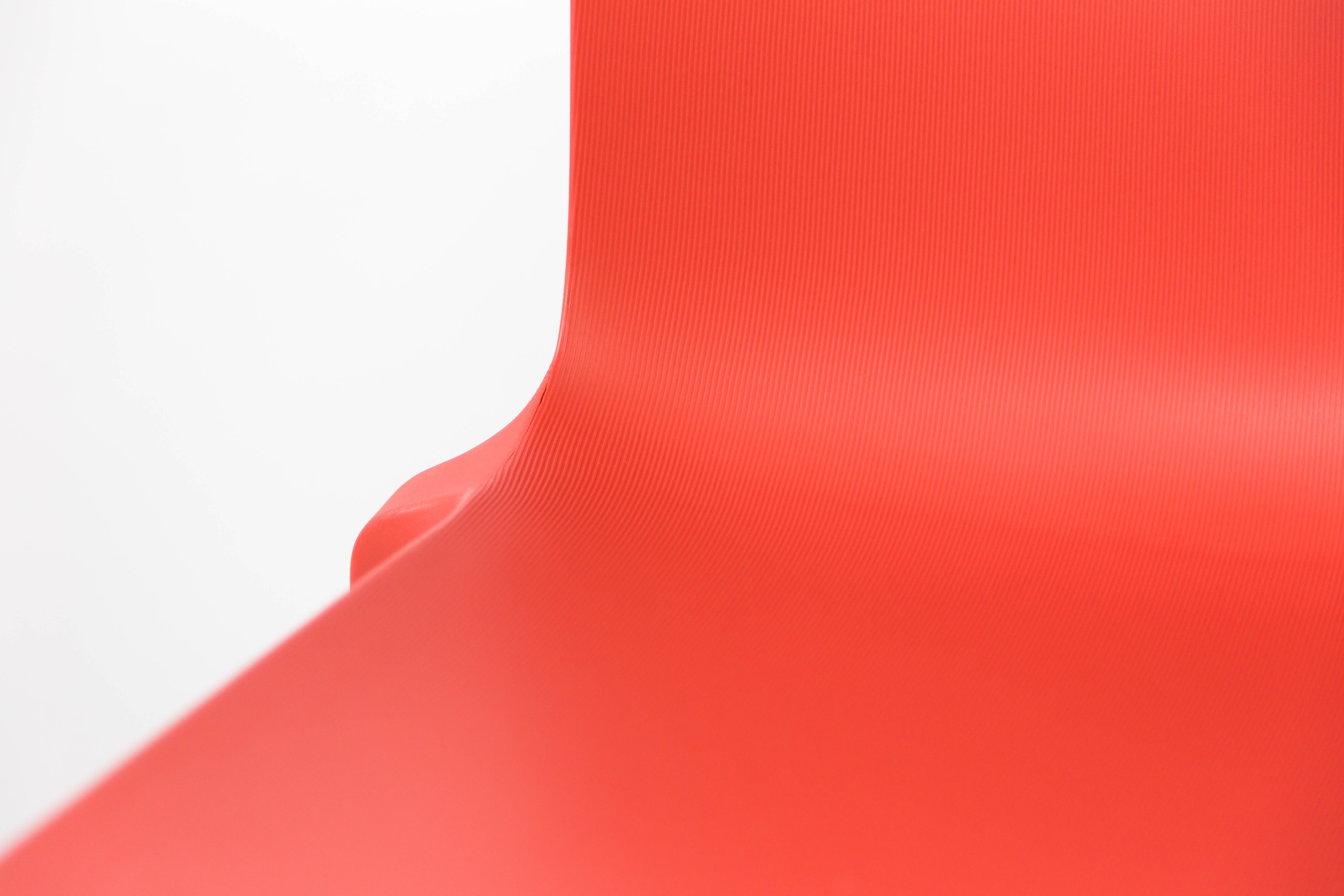 Gros plan sur la surface lisse et incurvée en polypropylène rouge de la Chaise Extérieur Indi Bellini Empilable de Monsieur Bureau, qui présente une texture horizontale subtile, parfaite pour les sièges d'extérieur professionnels.