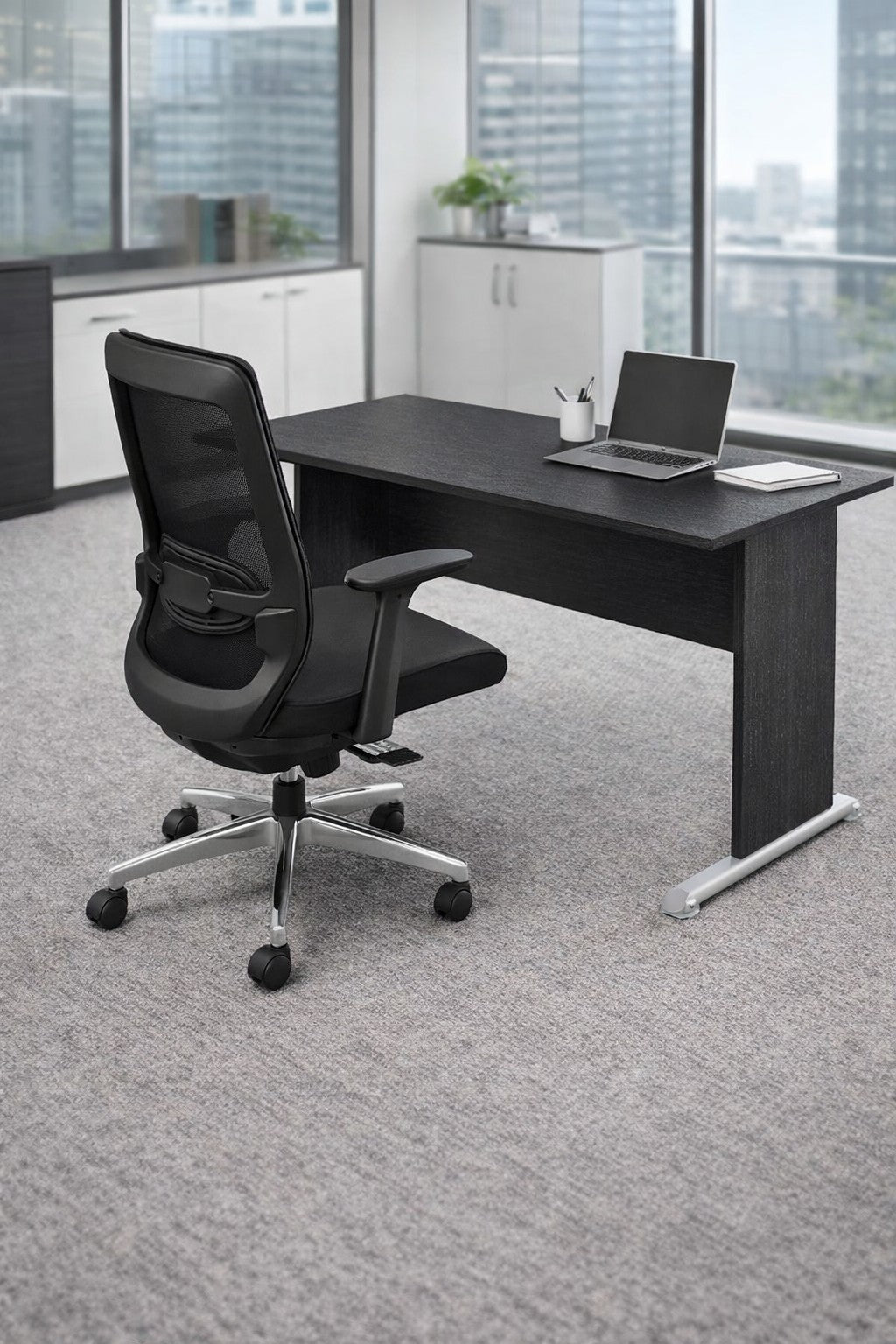 Un bureau moderne avec la Solution de bureau Budget Modulable Pieds L de Monsieur Bureau en noir, une chaise ergonomique, un ordinateur portable ouvert et un bloc-notes. De grandes fenêtres permettent de voir les bâtiments de la ville ; des armoires blanches bordent le mur.#combo_bureau_droit_frene_noir