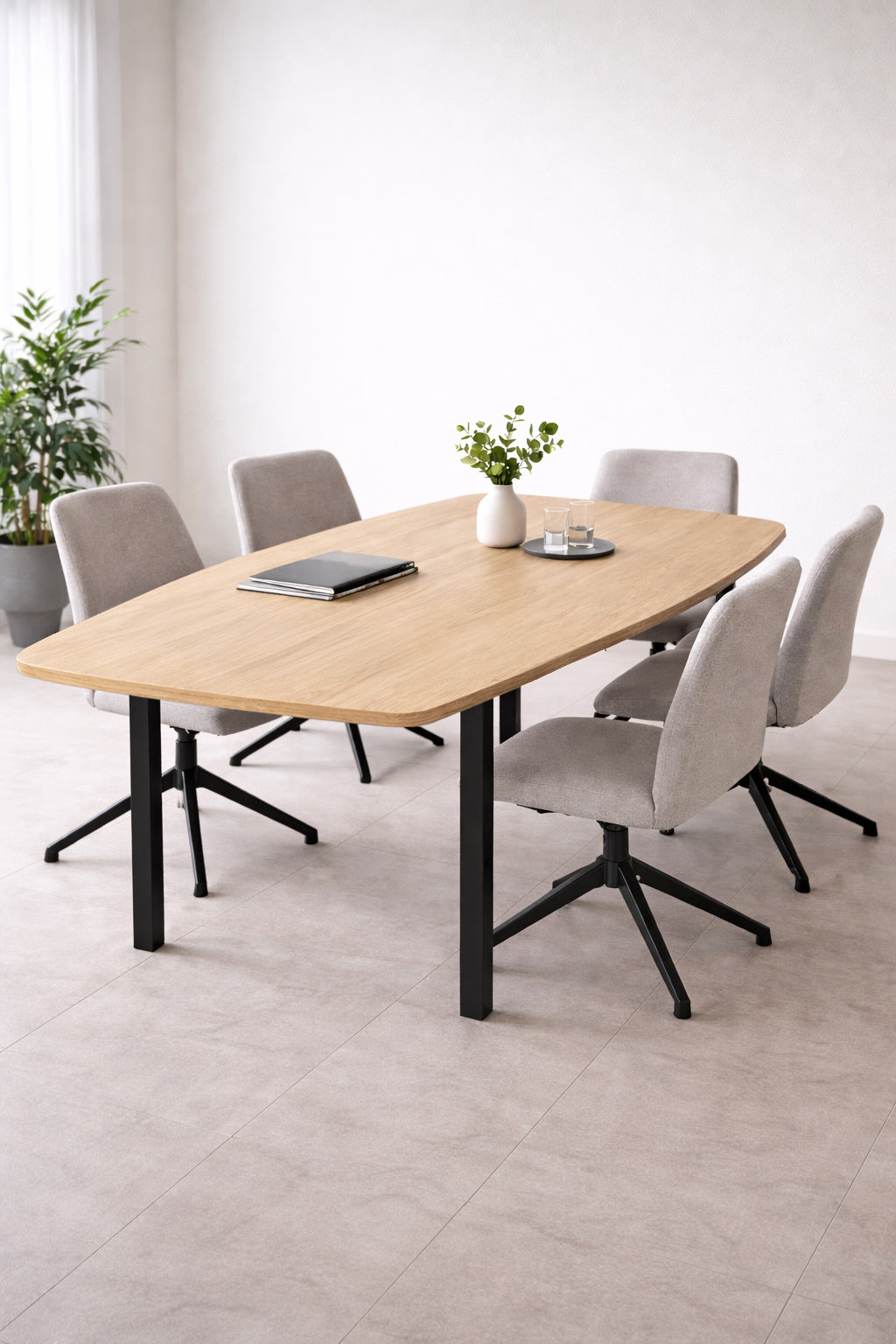 Une salle à manger moderne avec Monsieur Bureau Table de réunion tonneau professionnel Astral (6 pers), six chaises rembourrées grises, un carnet de notes, un stylo et deux petites plantes en pot. Une grande plante se trouve dans le coin et la lumière naturelle douce remplit l'espace..#combo_chene_nebraska_noir