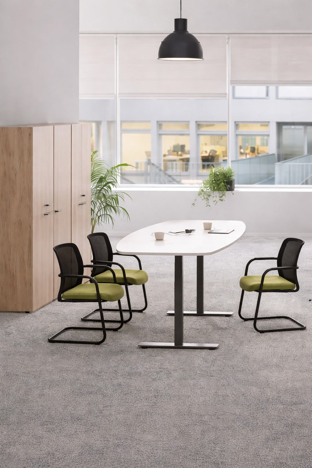 Un espace de réunion de bureau moderne avec un Monsieur Bureau Table tonneau électrique Top & Down - 6/8 personnes (blanc, réglable en hauteur), trois chaises noires avec des sièges verts, deux tasses, une plante en pot, des armoires en bois et de grandes fenêtres éclairées par le soleil..#combo_blanc_noir