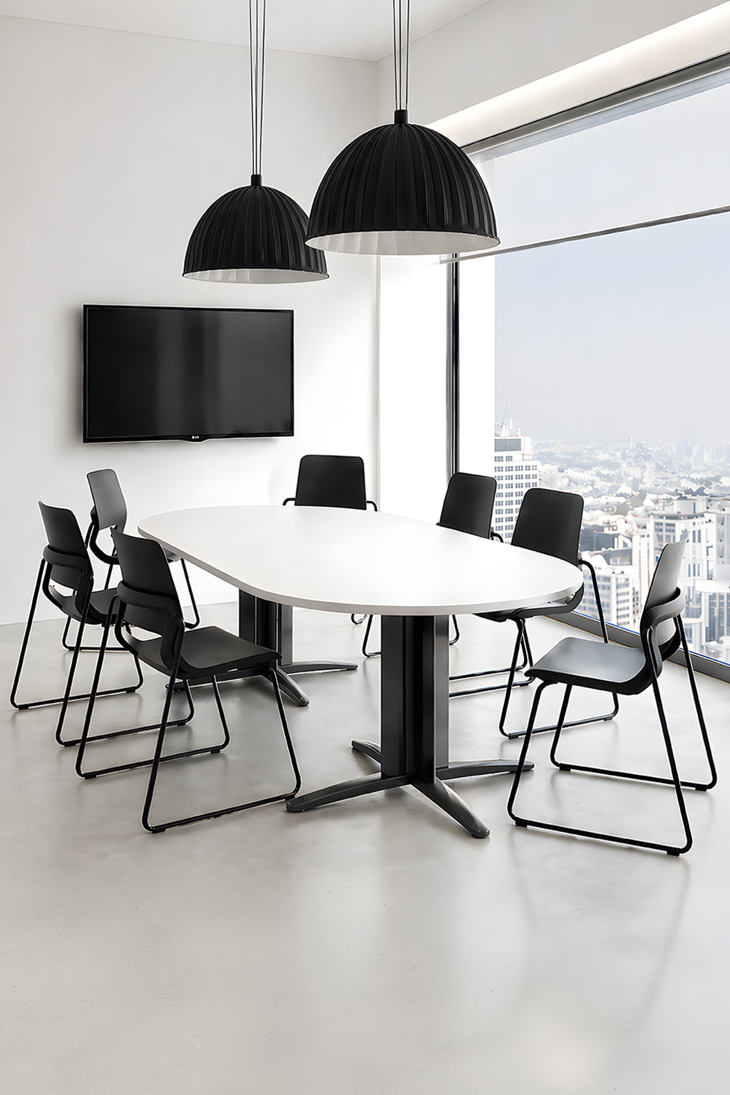 Une salle de réunion moderne avec une table de réunion ovale professionnelle Atlas de Monsieur Bureau, six chaises noires, deux grandes lampes suspendues noires, une télévision murale et de grandes fenêtres donnant sur la ville..#combo_blanc_noir