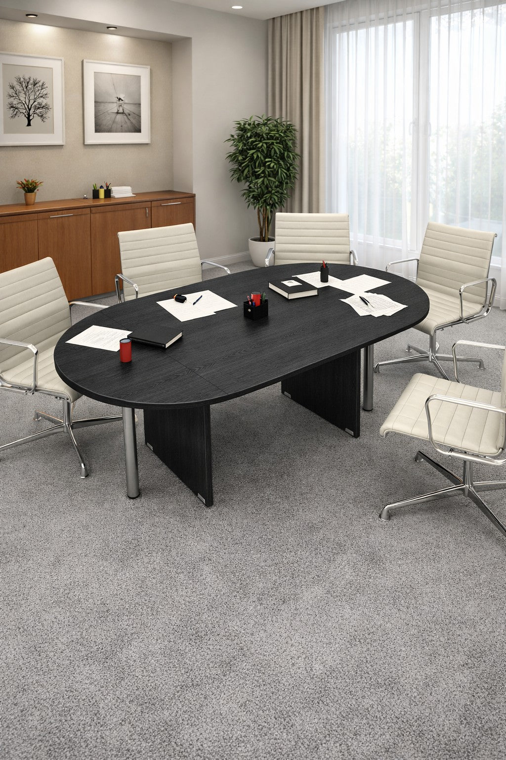 Une salle de conférence moderne présente la Table de réunion ovale Budget 6/8 personnes de Monsieur Bureau, six chaises blanches, des papiers, des cahiers, des stylos et une plante. De grandes fenêtres aux rideaux diaphanes éclairent des photos encadrées au-dessus d'élégants meubles de bureau en bois.#finitions_frene_noir