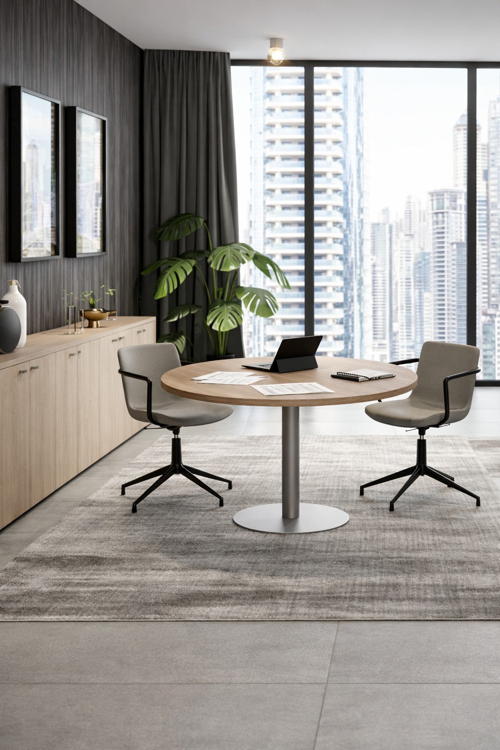 Un bureau moderne avec Monsieur Bureau Table de réunion ronde Ø 100/120 cm Curvy Express Plus, deux chaises, un ordinateur portable, des documents, de grandes fenêtres avec vue sur la ville, des armoires en bois, des œuvres d'art encadrées, une plante en pot et des tons gris élégants pour un aspect professionnel.#finitions_chene