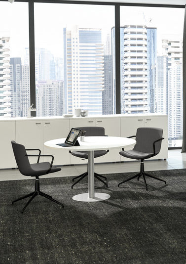 Un espace professionnel moderne avec Monsieur Bureau Table de réunion ronde Ø 100/120 cm Curvy Express Plus, trois chaises grises, une tablette sur la table, des armoires blanches, de grandes fenêtres et une vue sur les grands immeubles à l'extérieur.#finitions_blanc