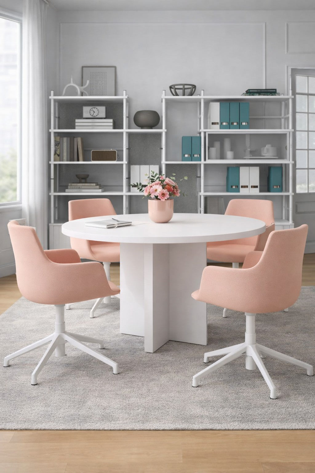 Une salle de réunion moderne est équipée de la Table de réunion ronde Olympe 4 à 6 personnes de Monsieur Bureau, de quatre chaises pivotantes roses, d'un vase à fleurs, d'étagères élégantes avec des livres et des objets de décoration, et de grandes fenêtres pour un mélange parfait de mobilier de bureau et de style.#finitions_blanc