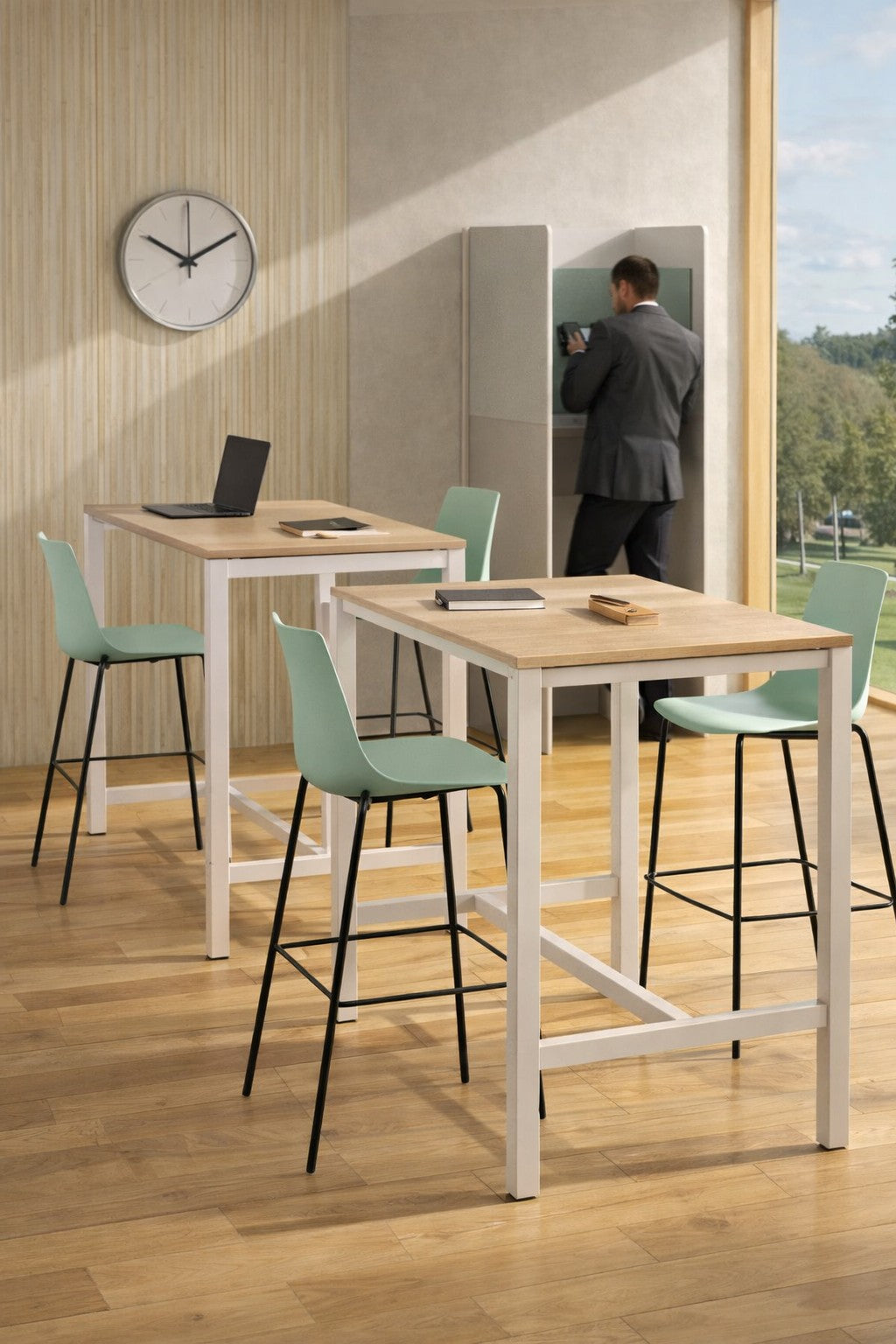 Bureau moderne avec un Monsieur Bureau Table Haute Astral (4-8 pers., 120-160 cm), des chaises vertes, des ordinateurs portables et des cahiers. Un homme en costume utilise une petite cabine téléphonique près de grandes fenêtres donnant sur la verdure ; horloge murale incluse.#combo_chene_fil_blanc