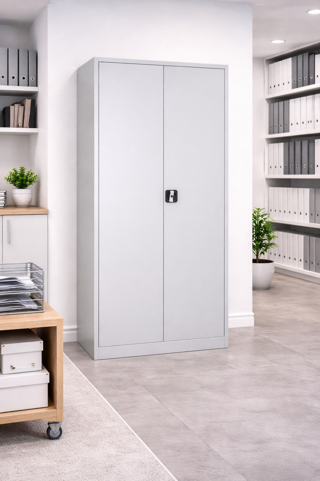 L'Armoire Haute Métal à portes battantes SOLID H180 cm de Monsieur Bureau, dotée d'une serrure, se dresse dans un bureau moderne parmi des classeurs bien rangés, une plante en pot et des meubles élégants sur un sol carrelé.