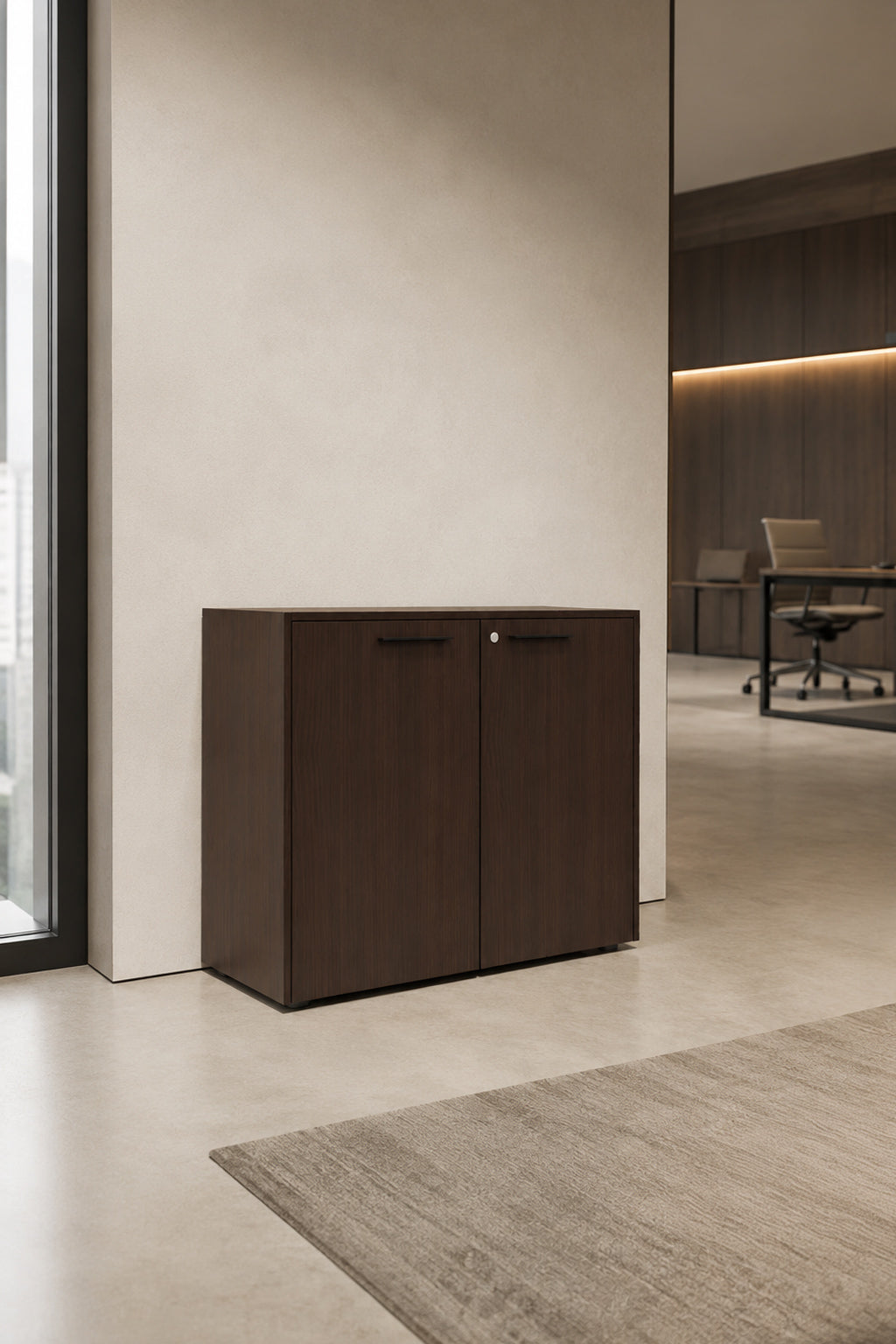 L'Armoire basse Passe Partout 2 portes de Monsieur Bureau (L90 x H79.5) est posée contre un mur clair dans un bureau moderne aux tons neutres et à la décoration minimale.#finitions_noyer