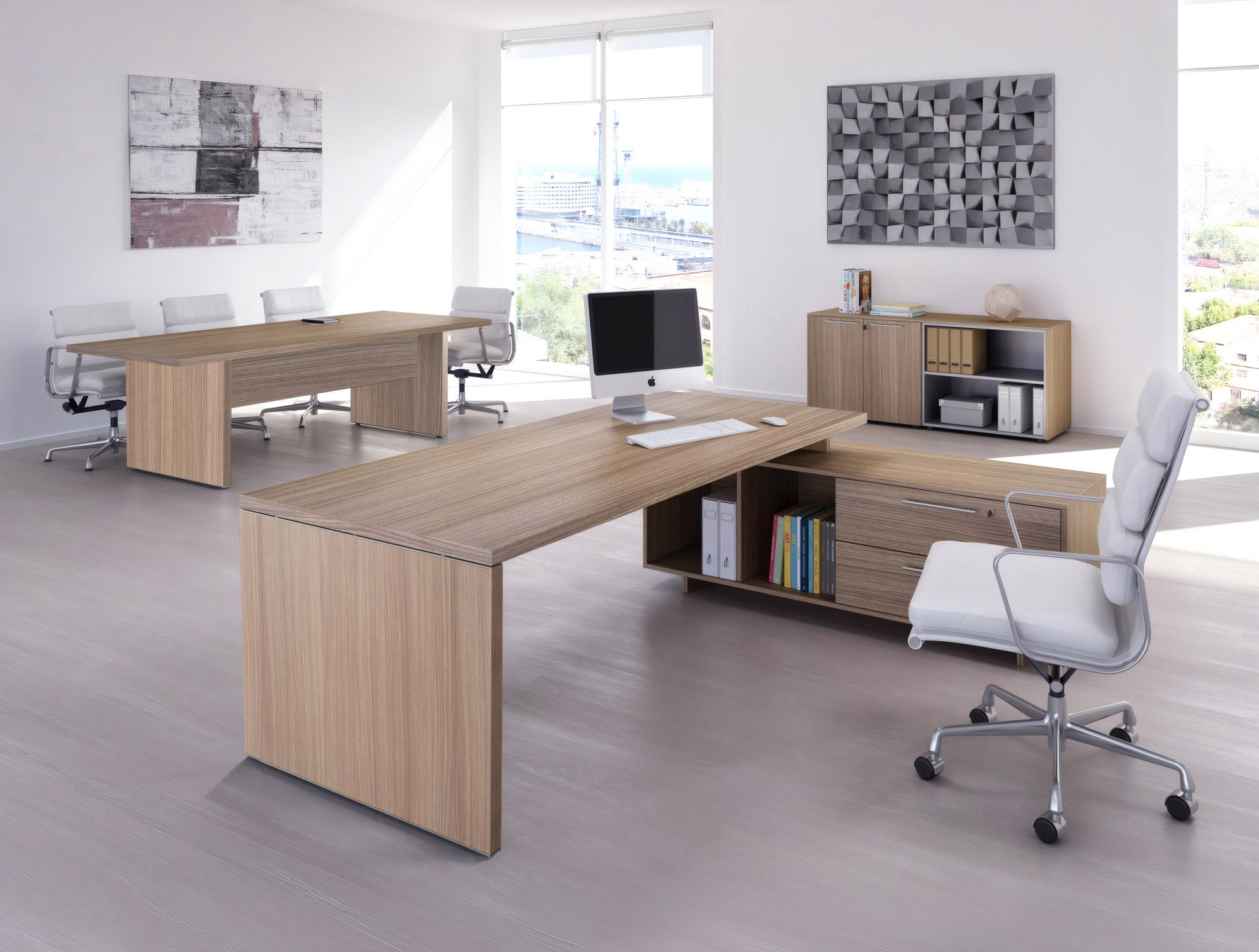Bureau moderne avec des meubles en bois clair, dont le Bureau de direction Flora sur console de Monsieur Bureau avec rangement intégré, des chaises blanches à roulettes, un ordinateur sur un bureau spacieux, des œuvres d'art sur des murs blancs et de grandes fenêtres remplies de lumière naturelle.