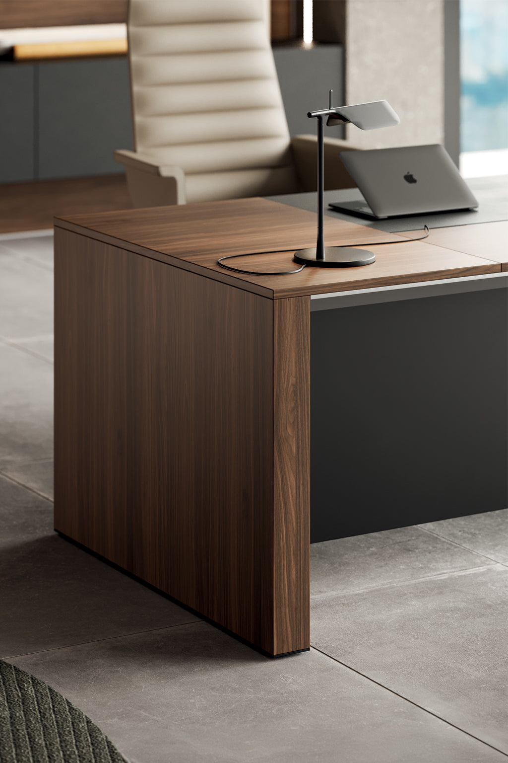 Le bureau de direction L200 ONO Monolithique en placage bois de Monsieur Bureau met en valeur une lampe élégante et un ordinateur portable fermé. Un fauteuil ergonomique beige se trouve derrière, face à des armoires et de grandes fenêtres.