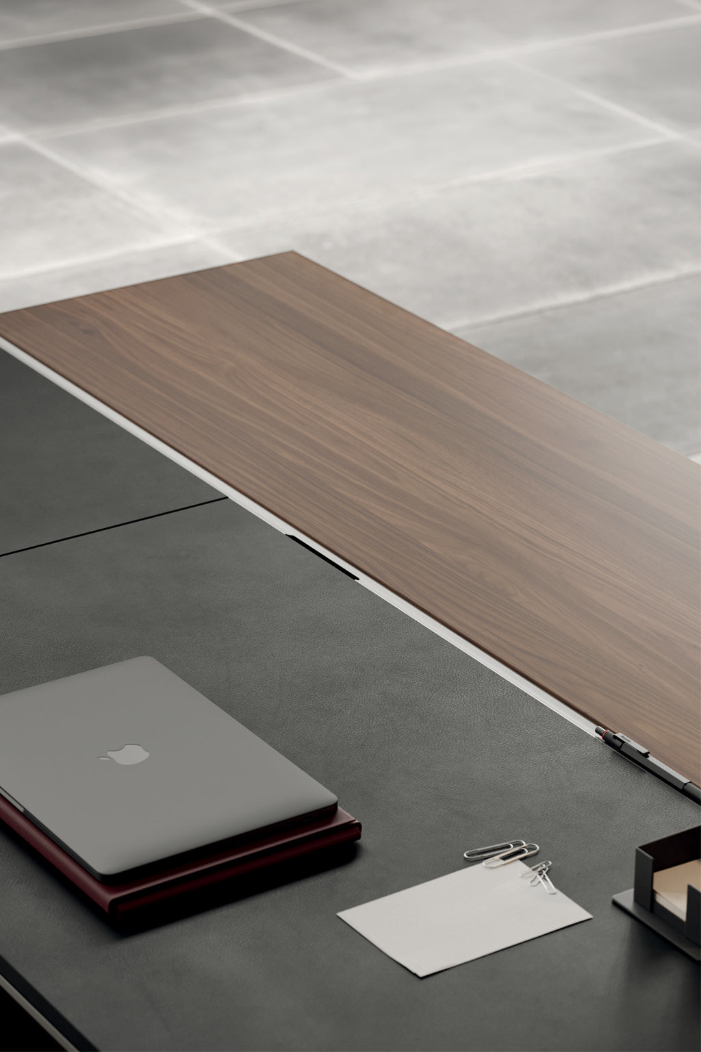 Le Bureau de direction L200 ONO Monolithique - Placage bois de Monsieur Bureau présente une installation minimaliste avec un ordinateur portable fermé, un bloc-notes avec trombones, un stylo et un organisateur de bureau en bois sur une surface noire et Noyer naturel sur un sol carrelé.