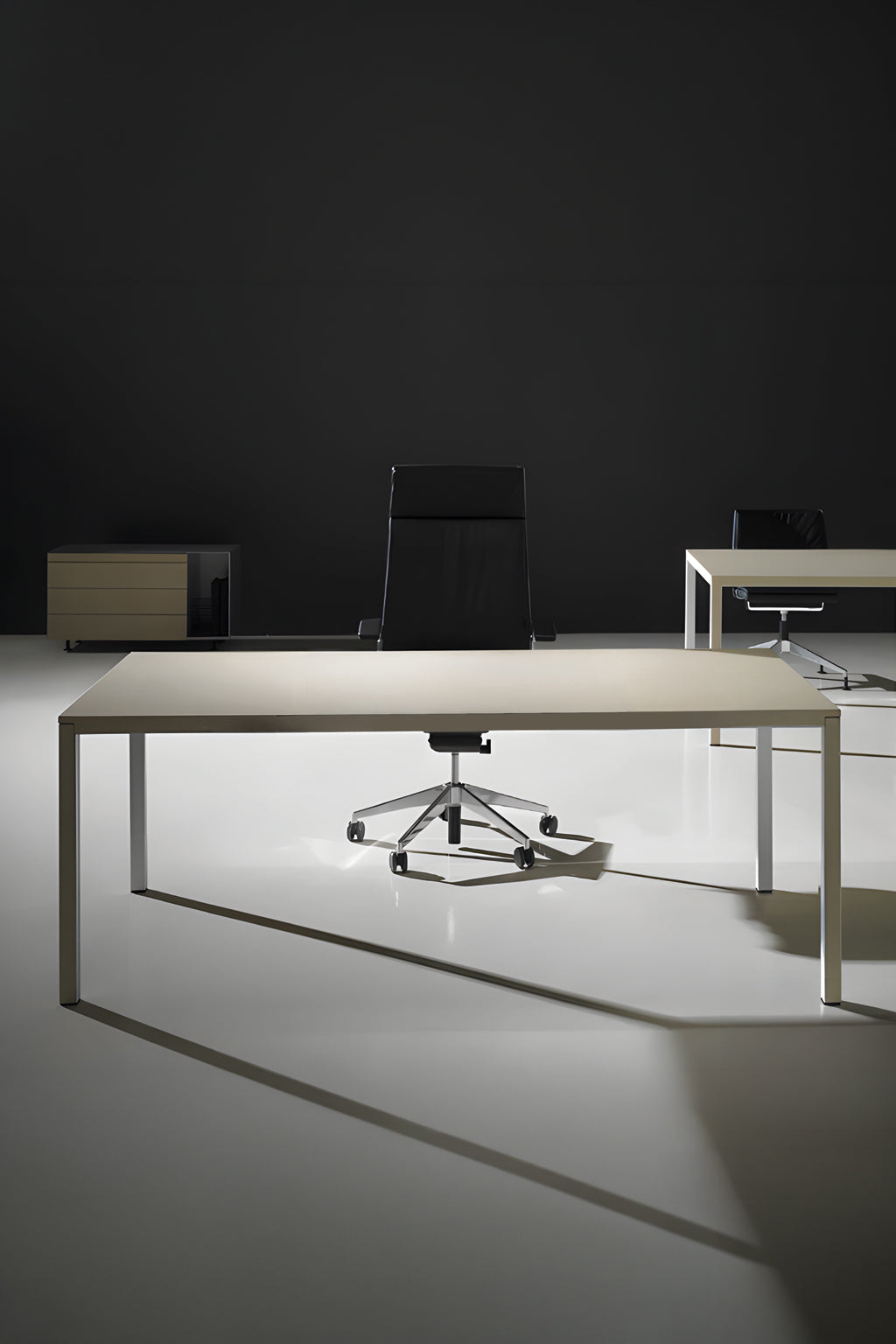 Un bureau minimaliste présente le Monsieur Bureau "Bureau de direction Nova" (L200 x P100 cm) dans des tons clairs et une chaise noire au centre. Un deuxième bureau, une chaise et une armoire apparaissent à l'arrière-plan, sur un mur sombre éclairé de façon spectaculaire.