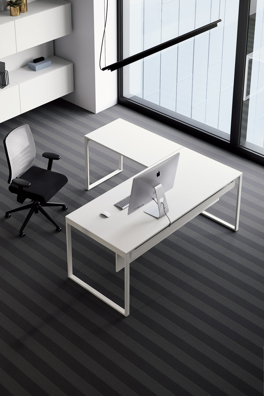 Un bureau moderne et minimaliste avec Monsieur Bureau Bureau de direction Pop Square avec retour, un ordinateur, une souris, une chaise de bureau noire, une moquette rayée, de grandes fenêtres et des étagères blanches avec des livres et de la décoration.
