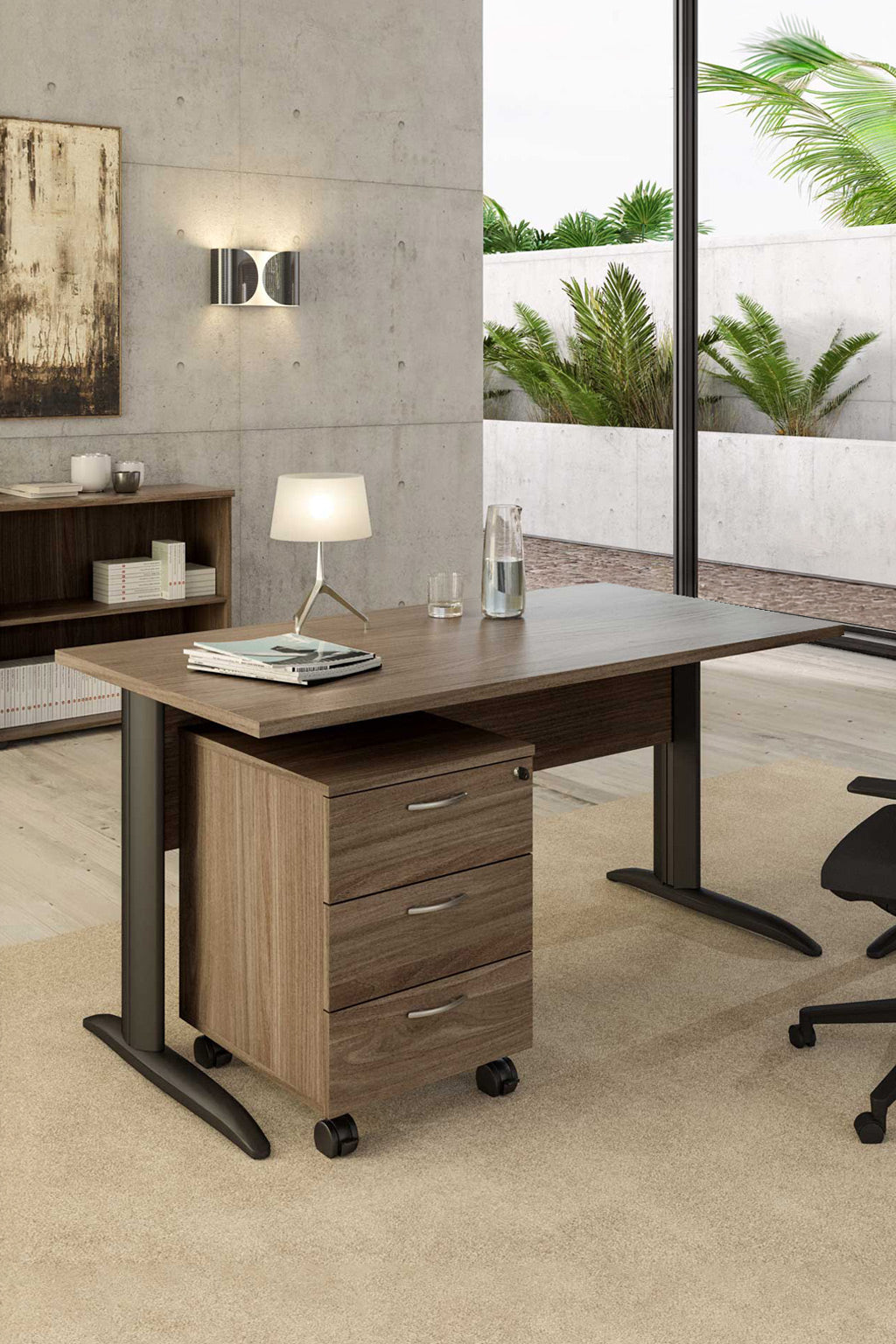 Un bureau moderne présente le Bureau Pro Effect Droit ou Angle Modulable de Monsieur Bureau, associé à un meuble mobile à trois tiroirs, une lampe de table, des livres, un carnet de notes et une bouteille d'eau en verre. De grandes fenêtres donnent sur des plantes vertes et des murs en béton..#combo_frene_de_toscane_anthracite