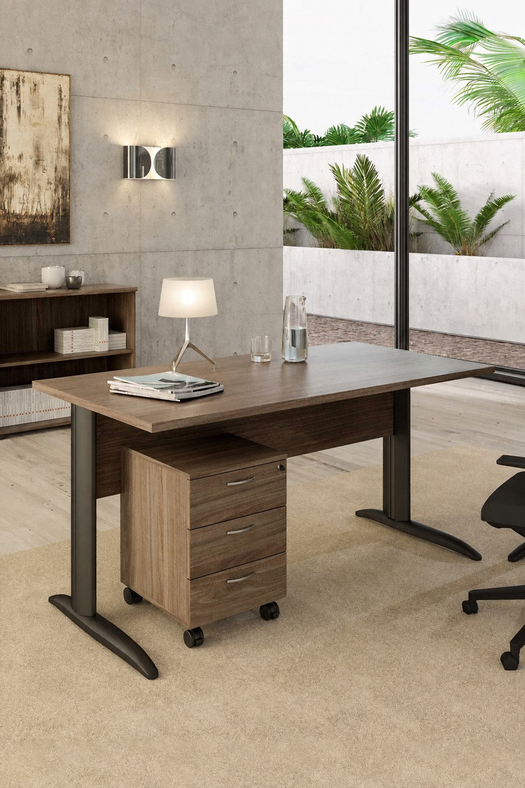 Un bureau moderne présente le Bureau Pro Effect Droit ou Angle Modulable de Monsieur Bureau, associé à un meuble mobile à trois tiroirs, une lampe de table, des livres, un carnet de notes et une bouteille d'eau en verre. De grandes fenêtres donnent sur des plantes vertes et des murs en béton..#combo_frene_de_toscane_anthracite