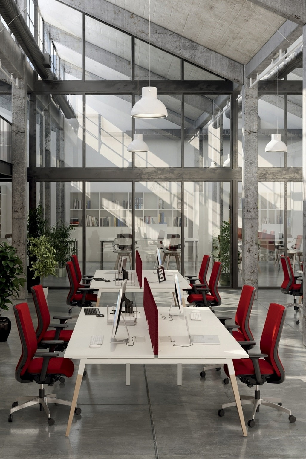 Un bureau moderne à aire ouverte avec des murs en béton, de grandes fenêtres et de hauts plafonds. Des rangées de Monsieur Bureau Bureau Bench OSLO pour 2 personnes P70 et 80 cm avec des chaises rouges et des séparateurs de bureau se font face, des ordinateurs sur chaque espace de travail ; des plantes vertes ajoutent au décor.#finitions_plateau_blanc