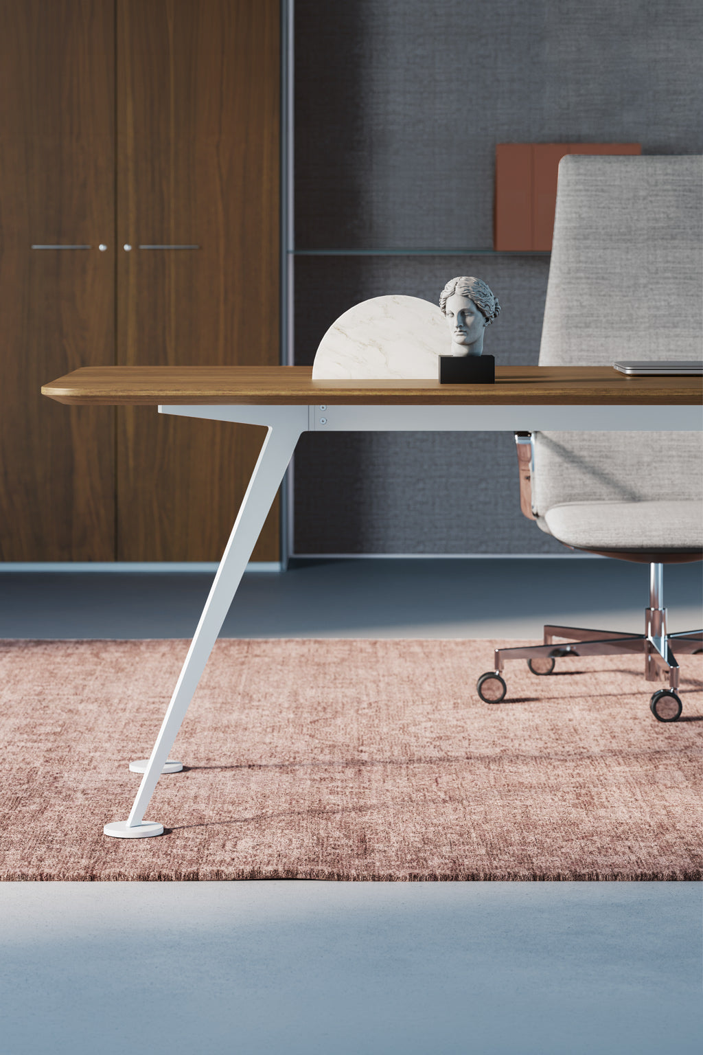 Le bureau de direction Spike conçu par Monsieur Bureau comprend un bureau en bois avec des pieds angulaires blancs, associé à une chaise de bureau grise sur roulettes. L'espace comprend une armoire en bois, un mur texturé, un tapis rose et une petite sculpture pour le style.