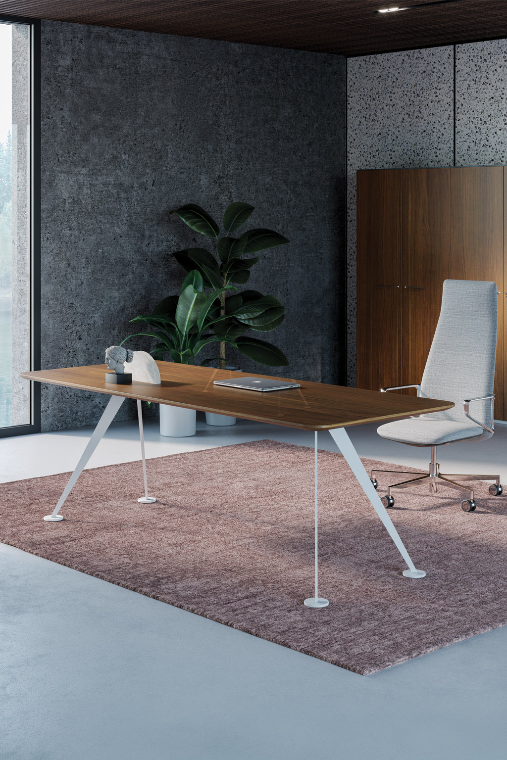 Le Bureau de direction Spike conçu par Monsieur Bureau présente un bureau en bois élégant, une chaise blanche à roulettes, une grande plante verte et une armoire en bois sur un mur gris texturé et un tapis rose discret.