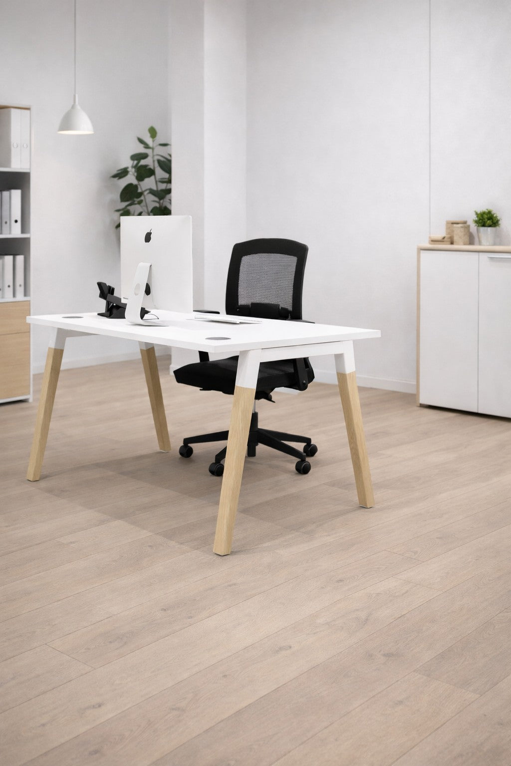 Le Bureau professionnel individuel Oslo P70 P80 cm de Monsieur Bureau est composé d'un bureau blanc, d'une chaise en maille noire et d'un ordinateur. Design scandinave avec des planchers en bois clair, des lignes épurées, des murs blancs, une plante, des armoires et des étagères pour un espace de travail moderne.