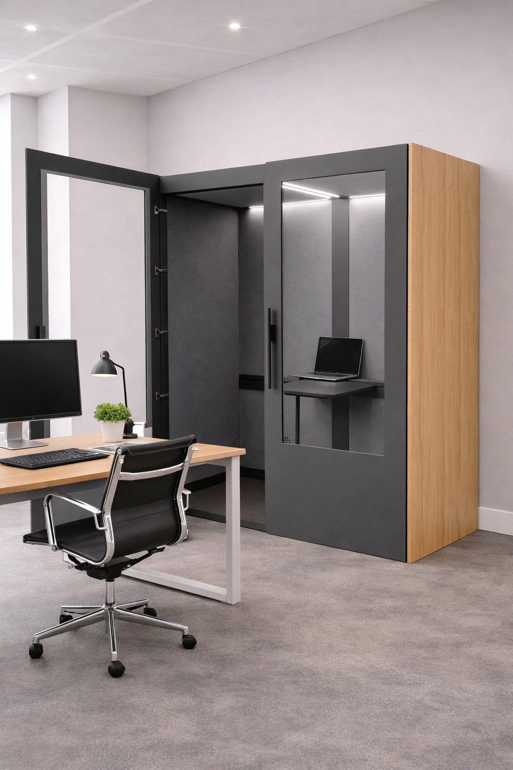 Un bureau moderne avec un bureau en bois, une chaise noire, un ordinateur de bureau et un Monsieur Bureau Cabine Acoustique Double No Sound Standard 2 pers avec des portes en verre, des panneaux en bois clair, un ordinateur portable et un éclairage zénithal.#finitions_chene