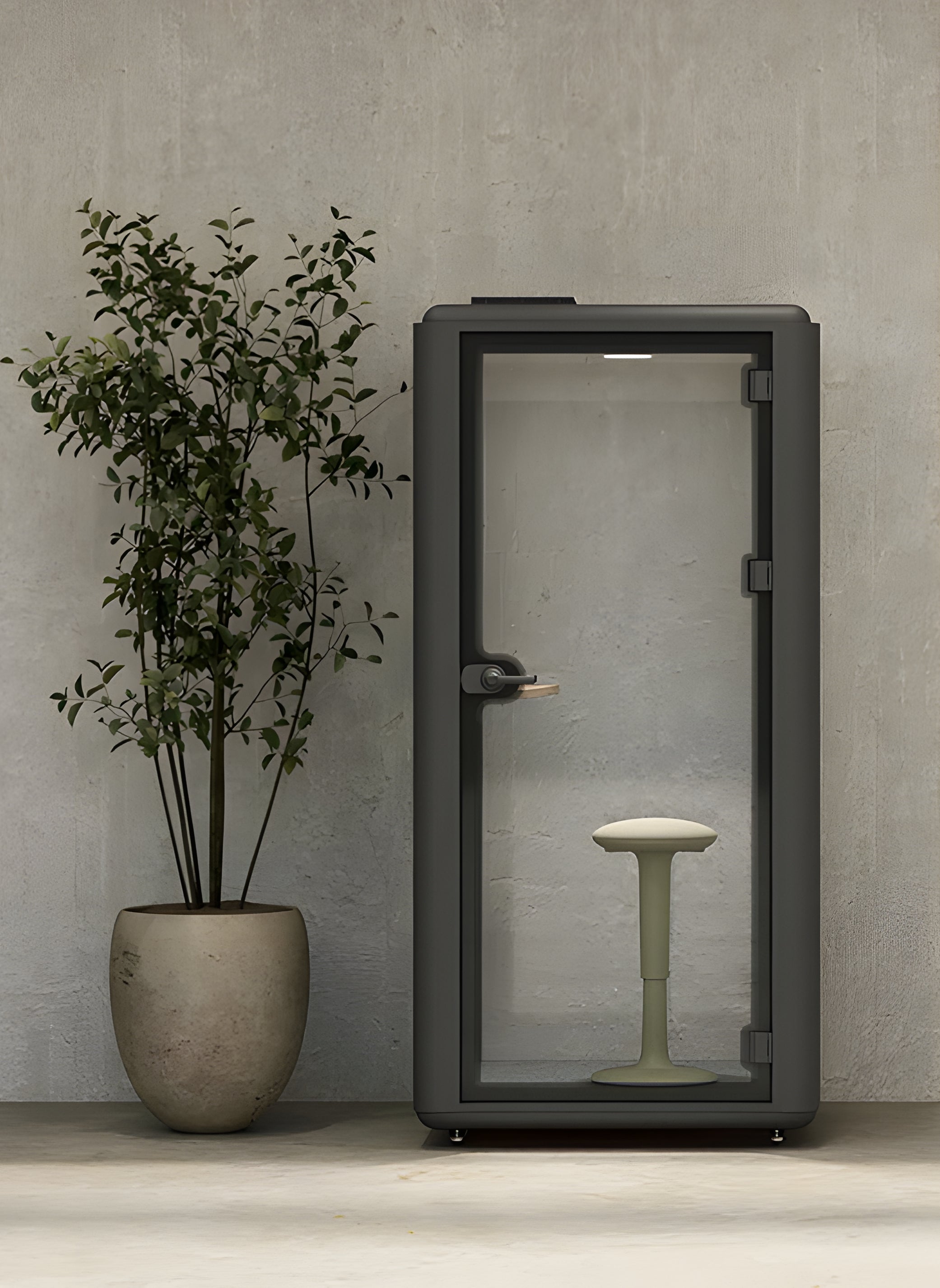 La Cabine acoustique Aura S - Phone Booth 1 pers de Monsieur Bureau, dotée d'une porte en verre et d'un tabouret simple, se trouve à côté d'une grande plante en pot contre un mur beige texturé, offrant une excellente isolation phonique.