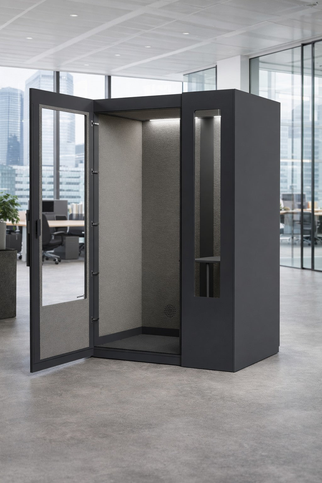 La Cabine acoustique de Travail NO SOUND Standard 1 pers de Monsieur Bureau, en gris foncé, se tient avec sa porte ouverte dans un bureau moderne et bien éclairé.#finitions_noir