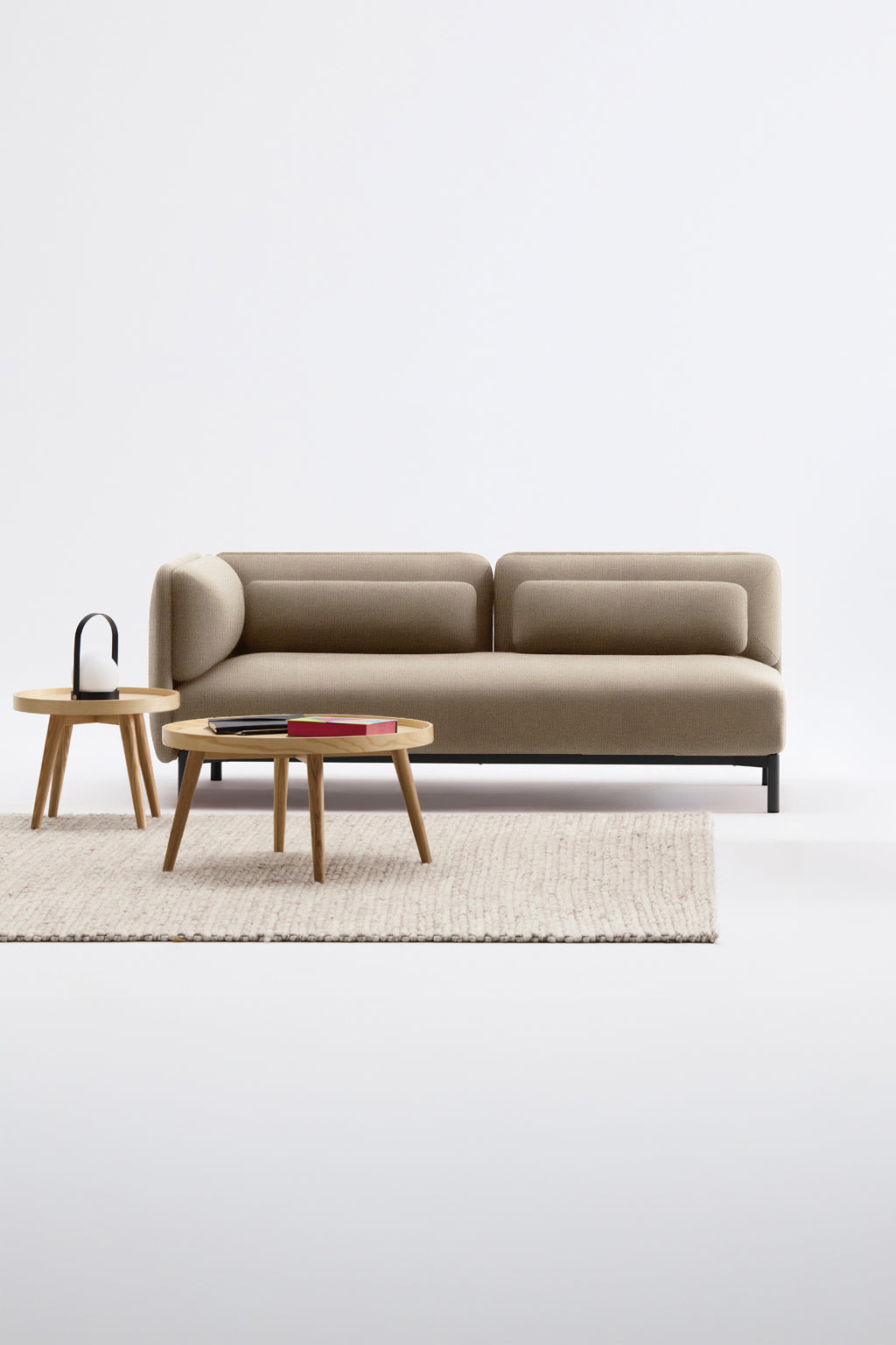 Un salon moderne présente le Canapé d'accueil modulaire Aurea - 1 accoudoir de Monsieur Bureau - un canapé marron avec deux tables rondes en bois, un livre et une lampe sur un tapis texturé clair sur un fond blanc uni.#finitions_beige